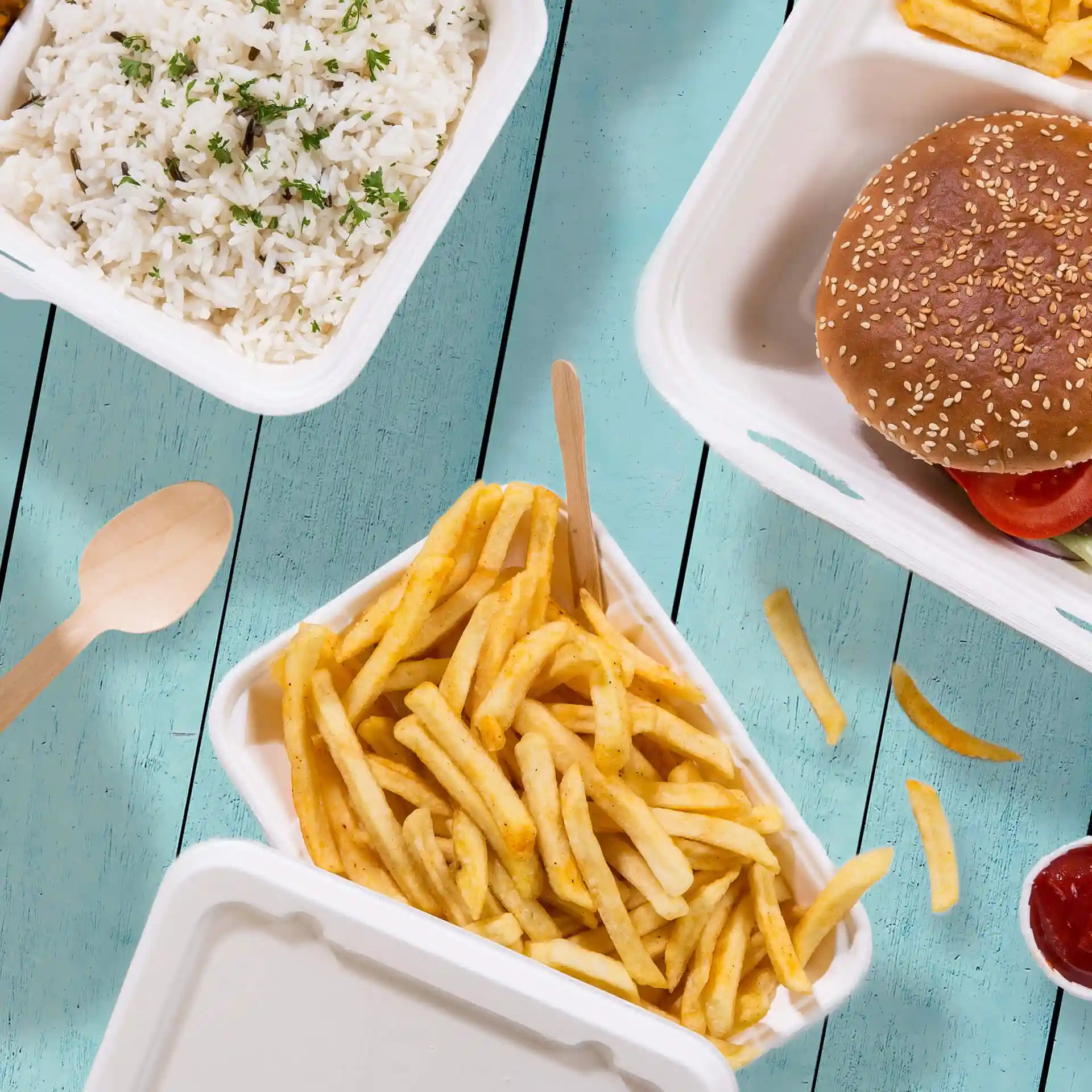 Image of a white rectangular bowl containing French fries, with a wooden spoon beside it on a blue wooden surface.