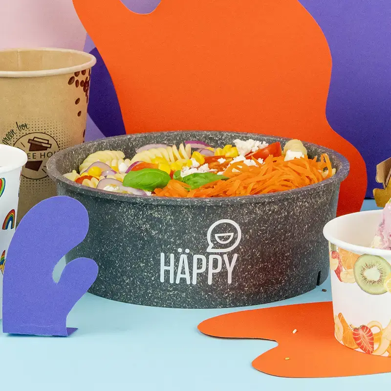 Brown bowl filled with salad, featuring a clear lid, placed on a wooden board with vegetables in the background.