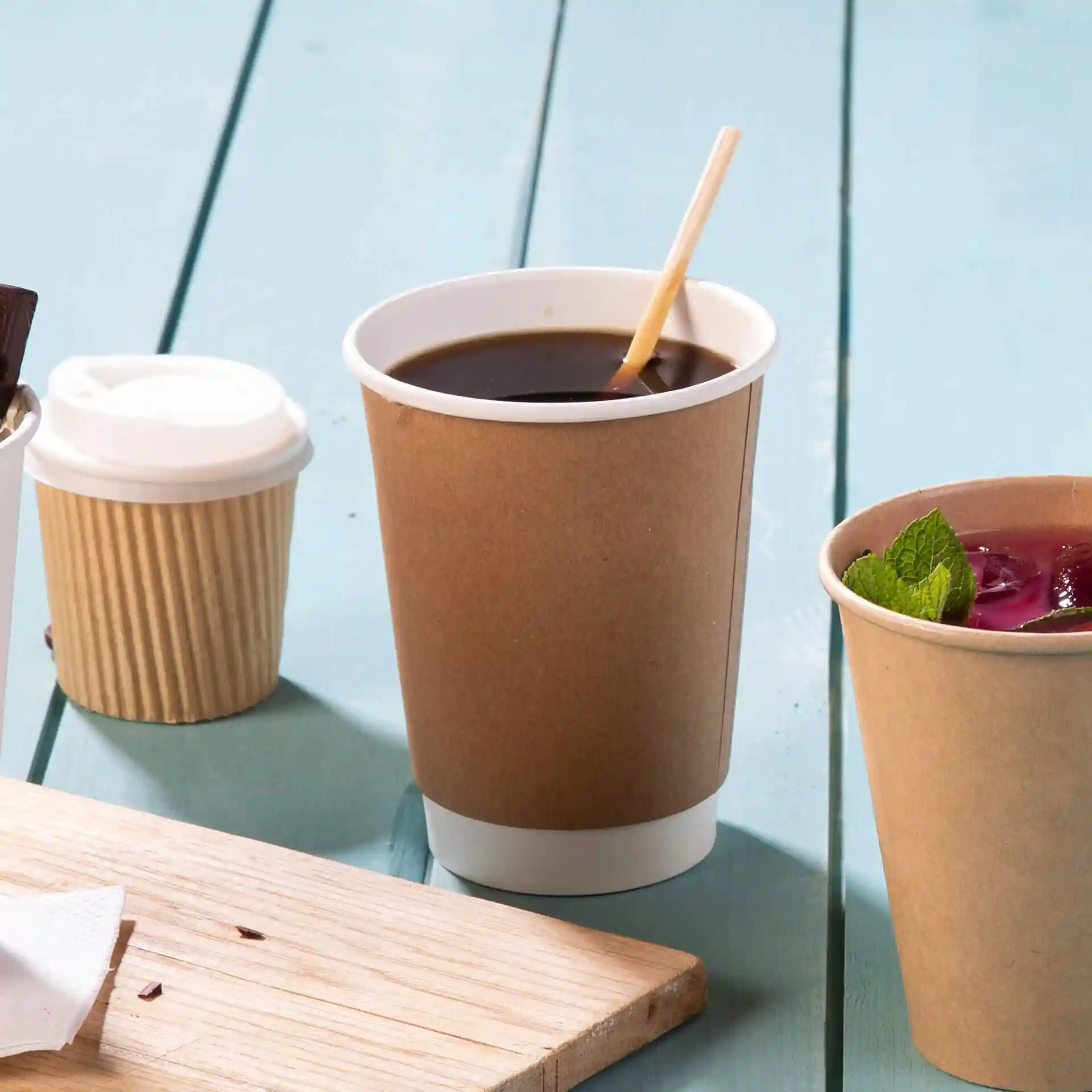Brown double-walled cardboard coffee cup with a white inner lining, filled with dark coffee and a wooden stirrer.
