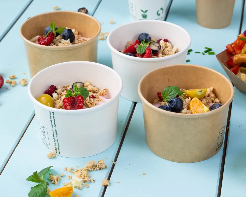 Four food containers filled with granola and fresh fruit, including berries and citrus, on a blue wooden surface.
