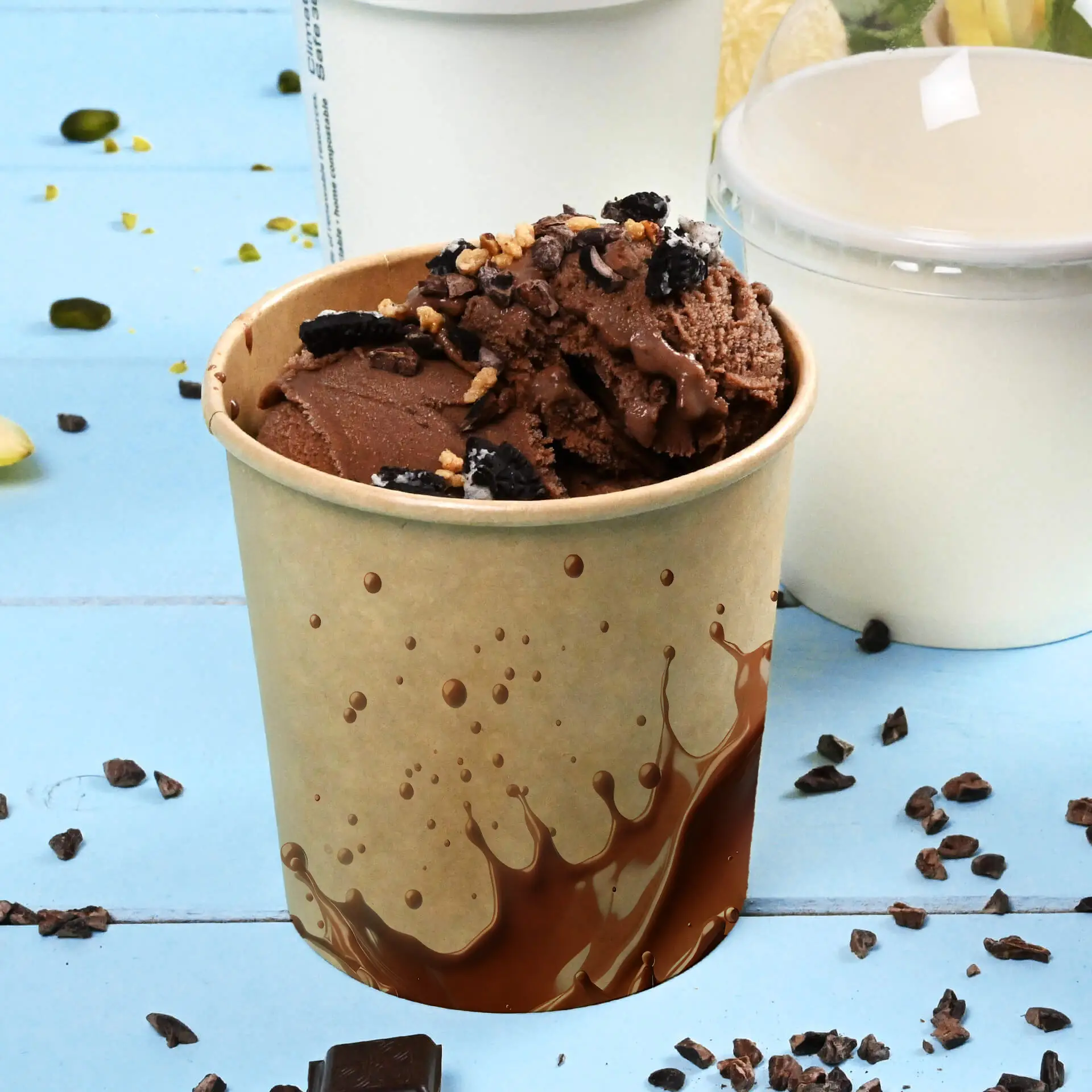 Cup filled with chocolate ice cream topped with toppings, placed on a blue surface with scattered chocolate pieces.