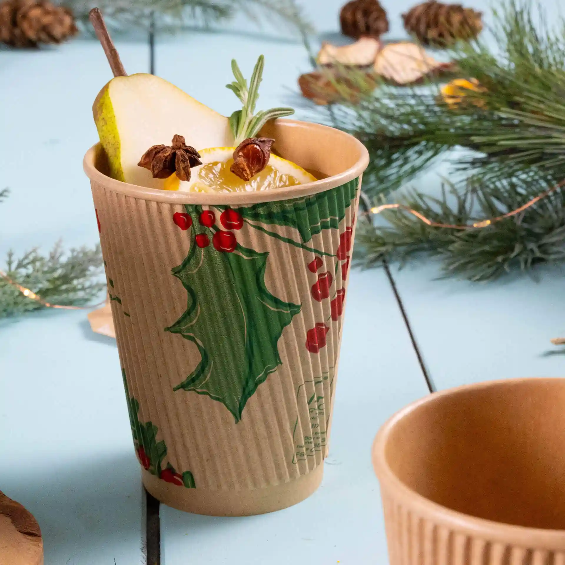 12 oz unbleached cardboard ripple cup with winter-themed design, filled with fruit and herbs, on a blue surface.