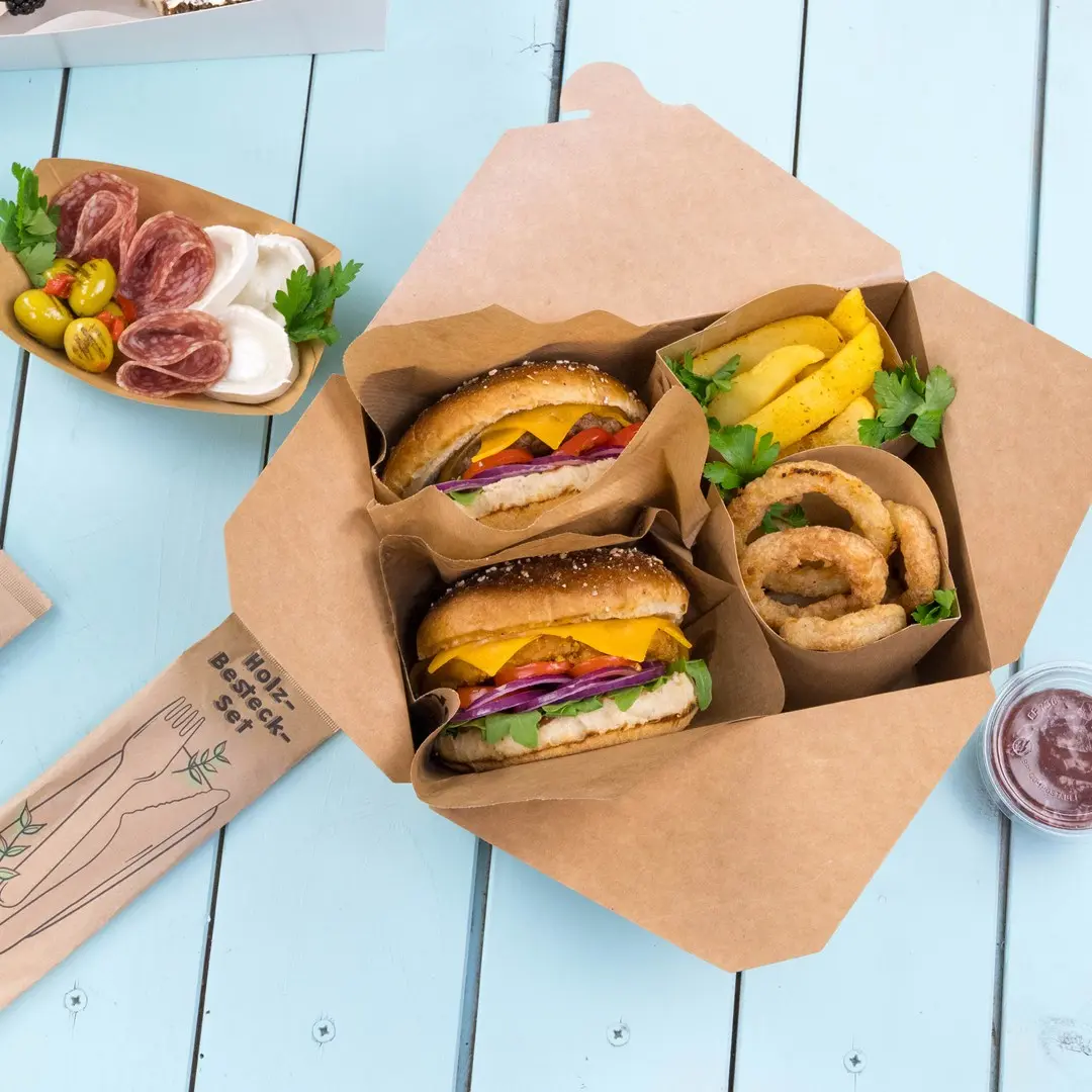 Takeaway box containing two burgers, onion rings, potato wedges, and a small container of sauce on a blue wooden surface.