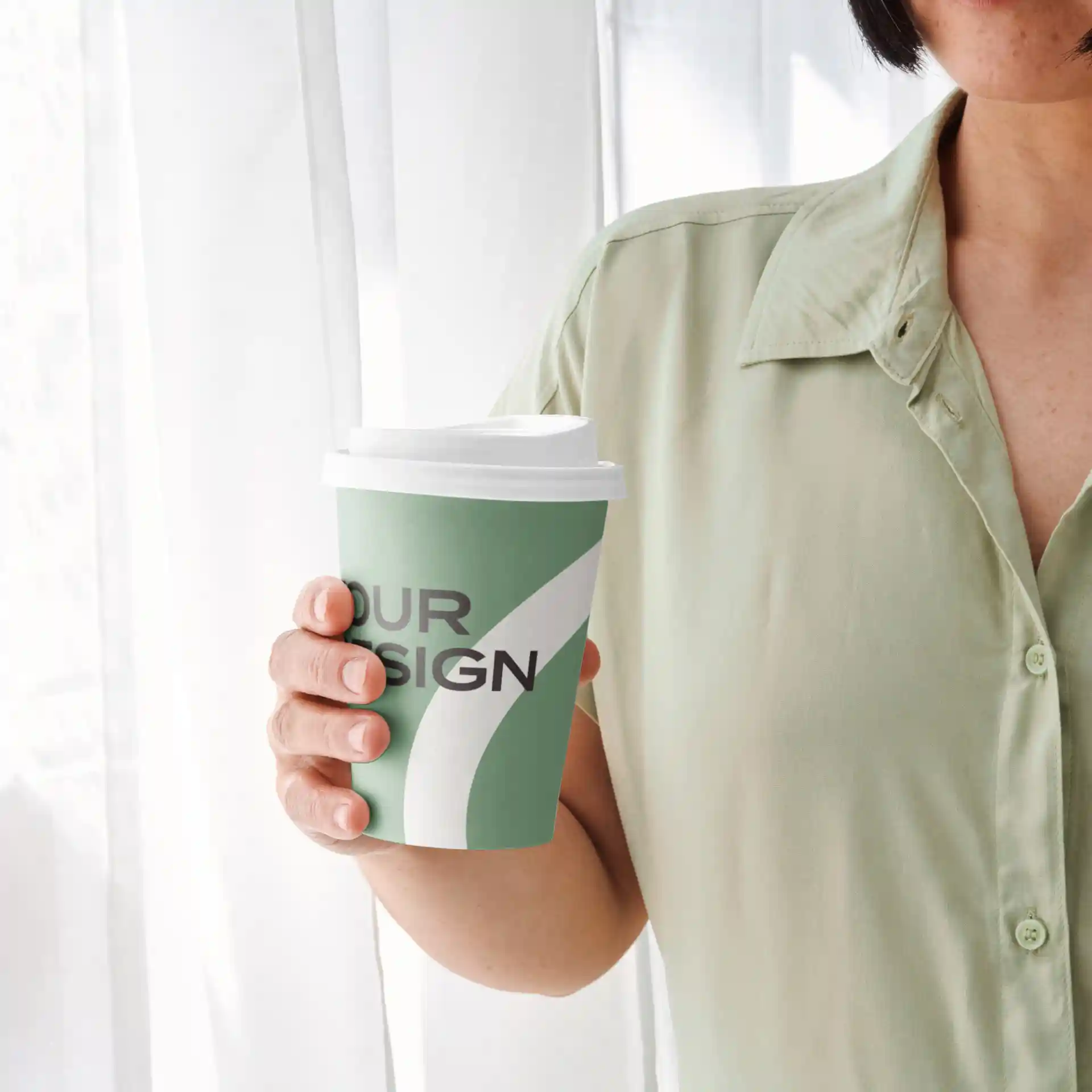 Green paper cup with a white lid, featuring a design and held by a person in a light green shirt.