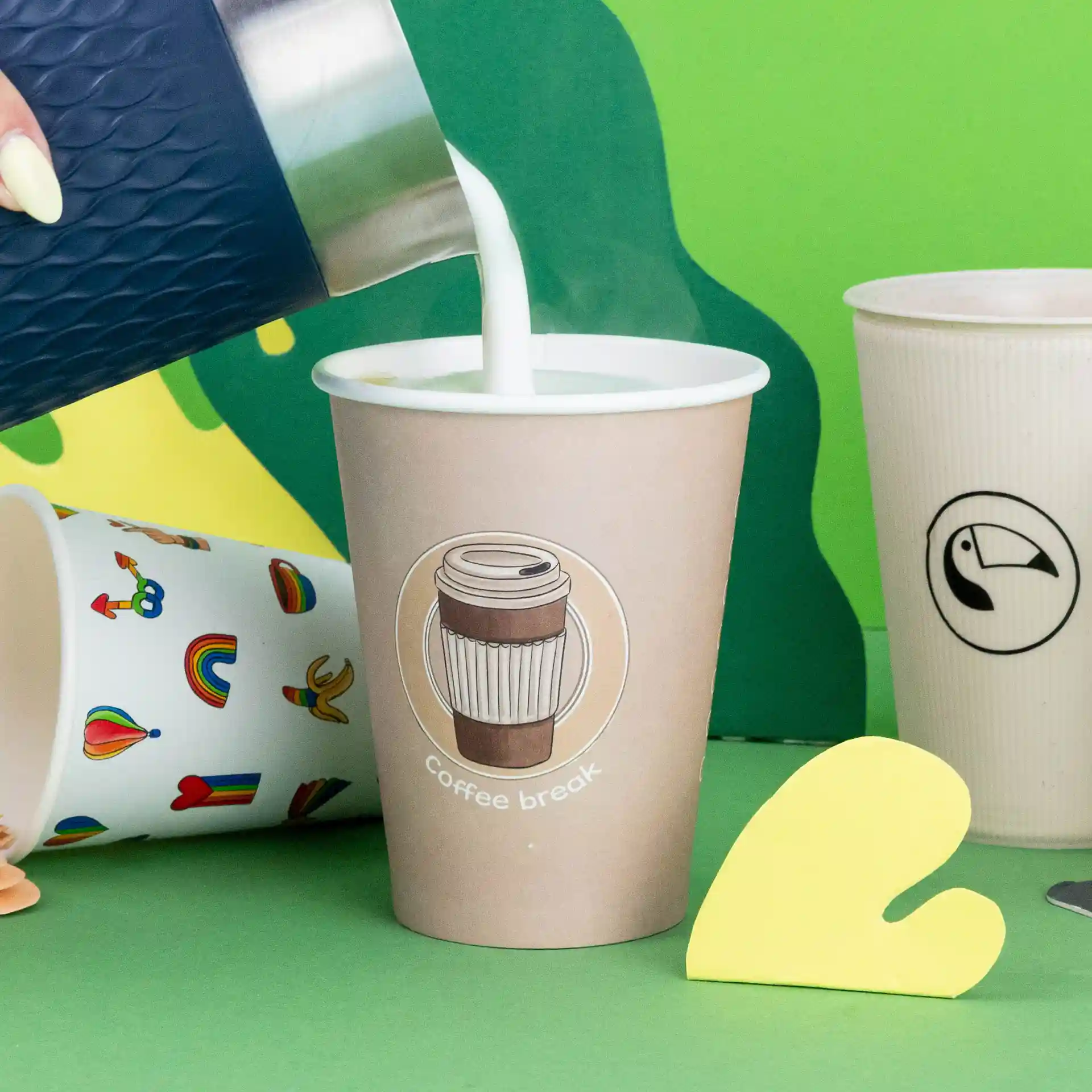 Image of a paper cup with a "coffee break" logo, being filled with milk, surrounded by other cups on a colorful background.