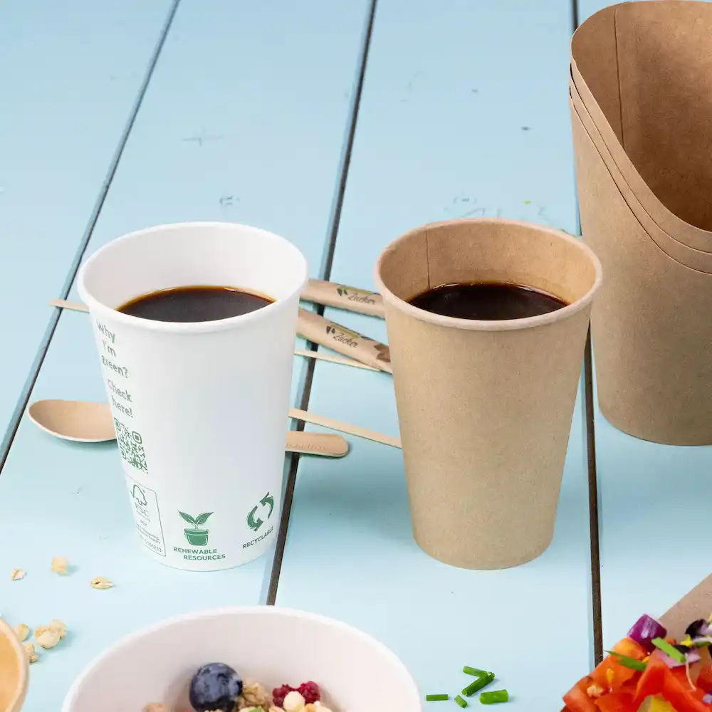 Two cups with coffee, one white and the other brown, beside wooden stirrers on a blue surface.
