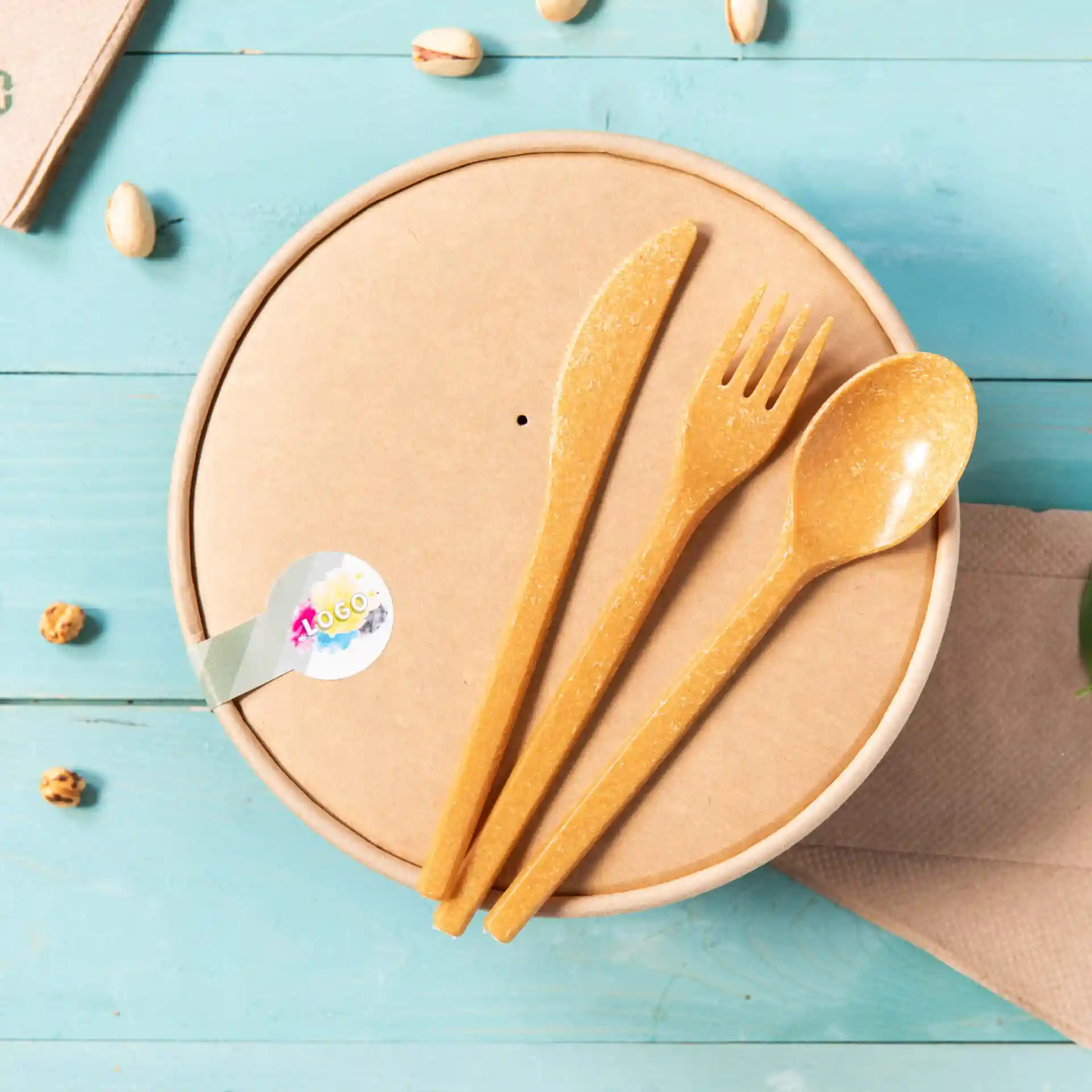 Round brown cardboard container with a lid, featuring three yellow utensils: a knife, fork, and spoon.