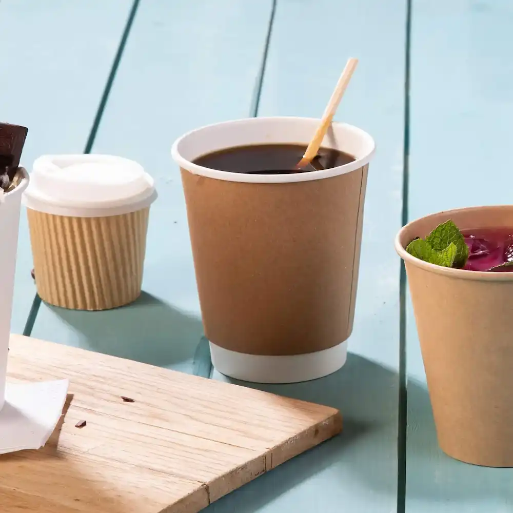 Brown double-walled paper cup with hot beverage, surrounded by a small container and a cup with mint garnish.