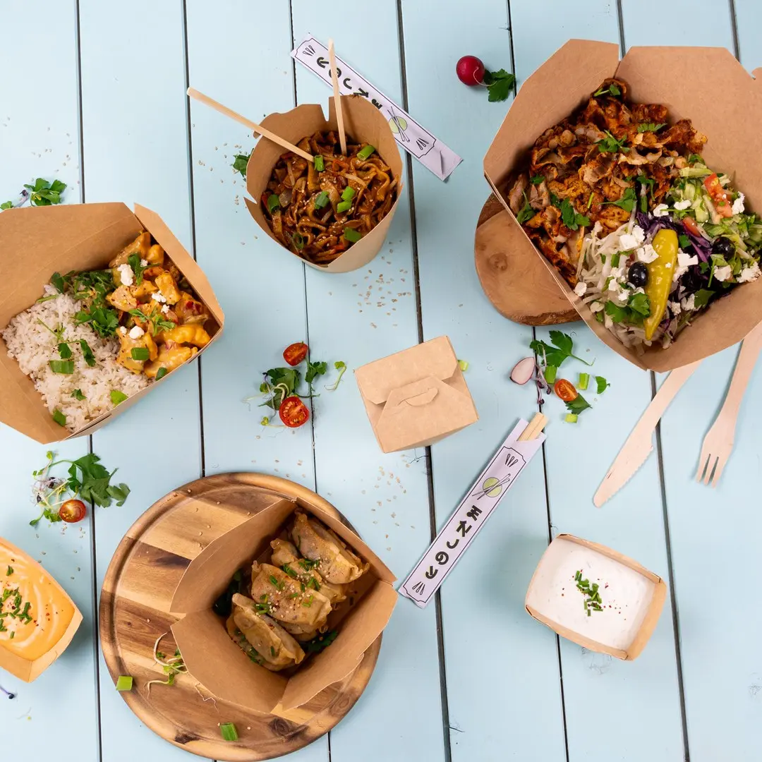 Assorted take-away food containers with noodles, rice, salad, and dumplings on a blue wooden surface.
