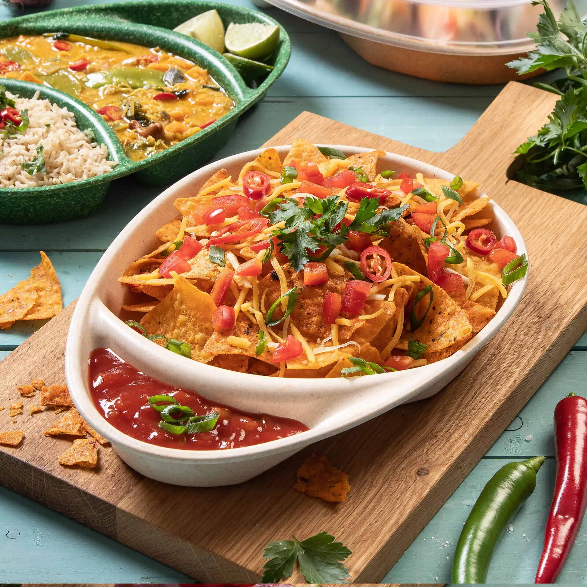 One bowl of nachos topped with cheese, tomatoes, and cilantro; served with salsa on a wooden platter. Additional dishes in the background.