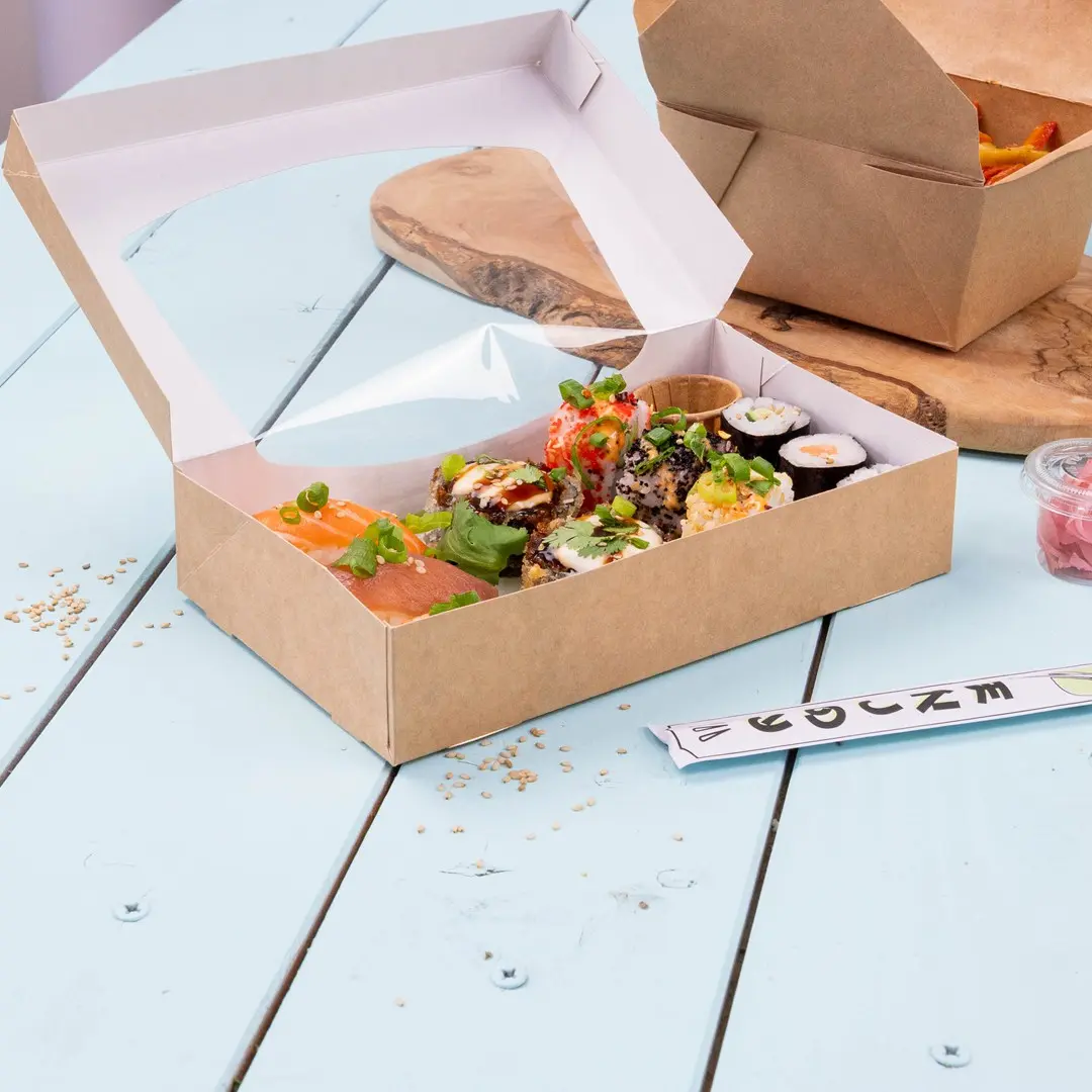Sushi box containing various sushi rolls, salmon, and garnishes, placed on a light blue wooden surface.