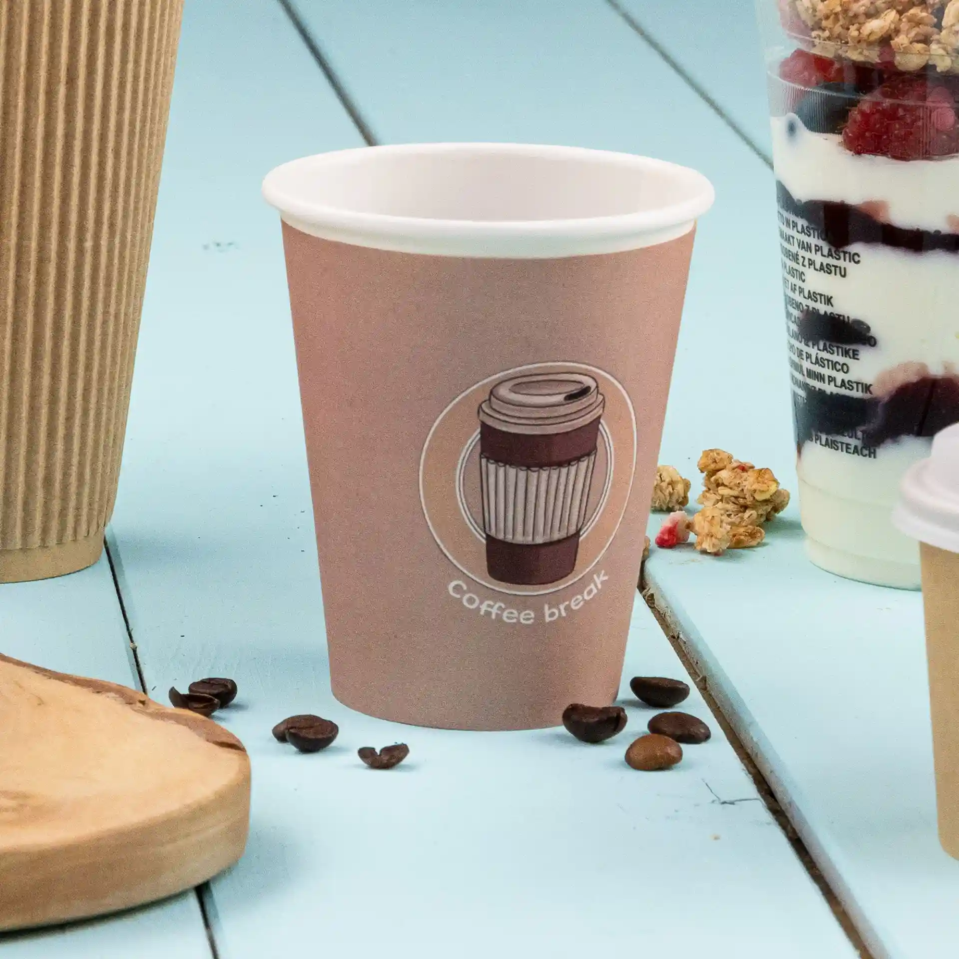 Brown paper cup with a printed coffee design and text, placed on a blue surface with coffee beans nearby.