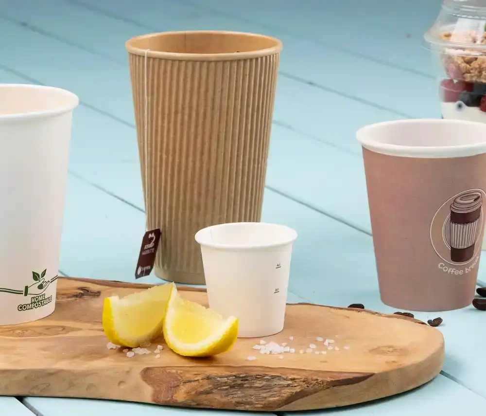 Assorted paper cups on a wooden surface with lemon wedges and salt crystals.
