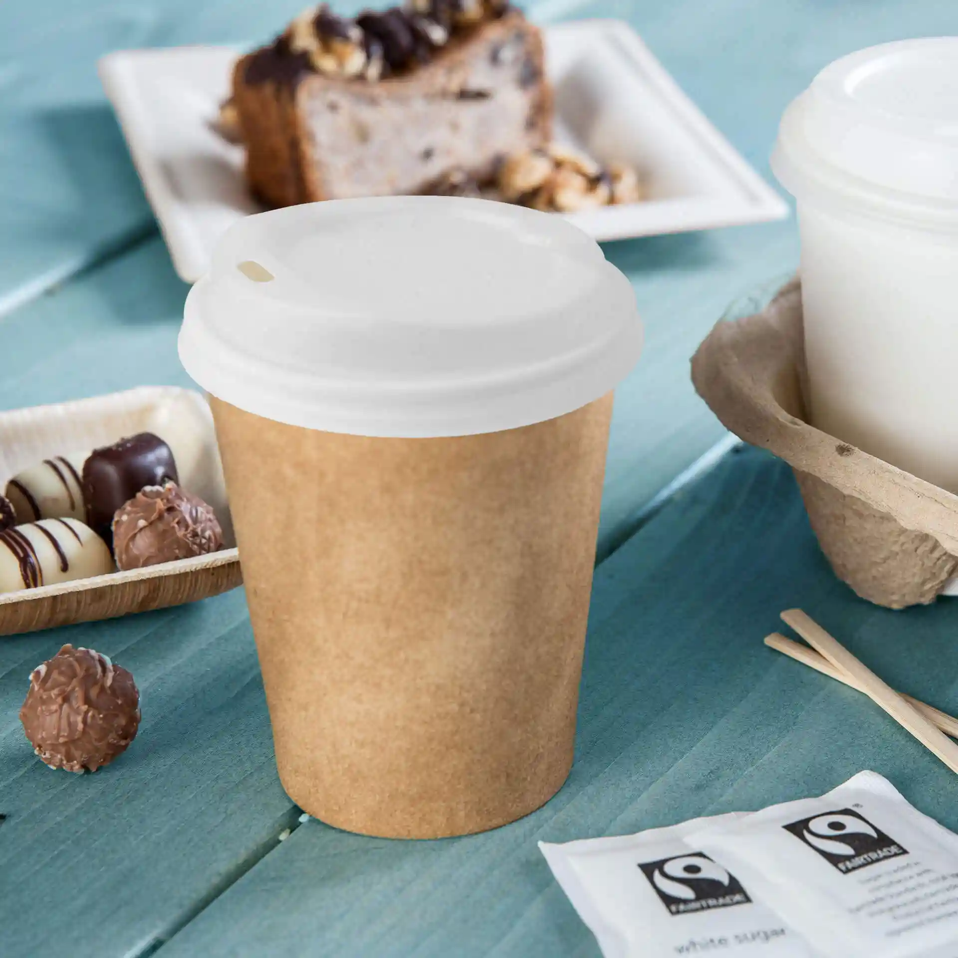 White PS lid with a drinking hole, designed for a round container, placed next to a brown paper cup.