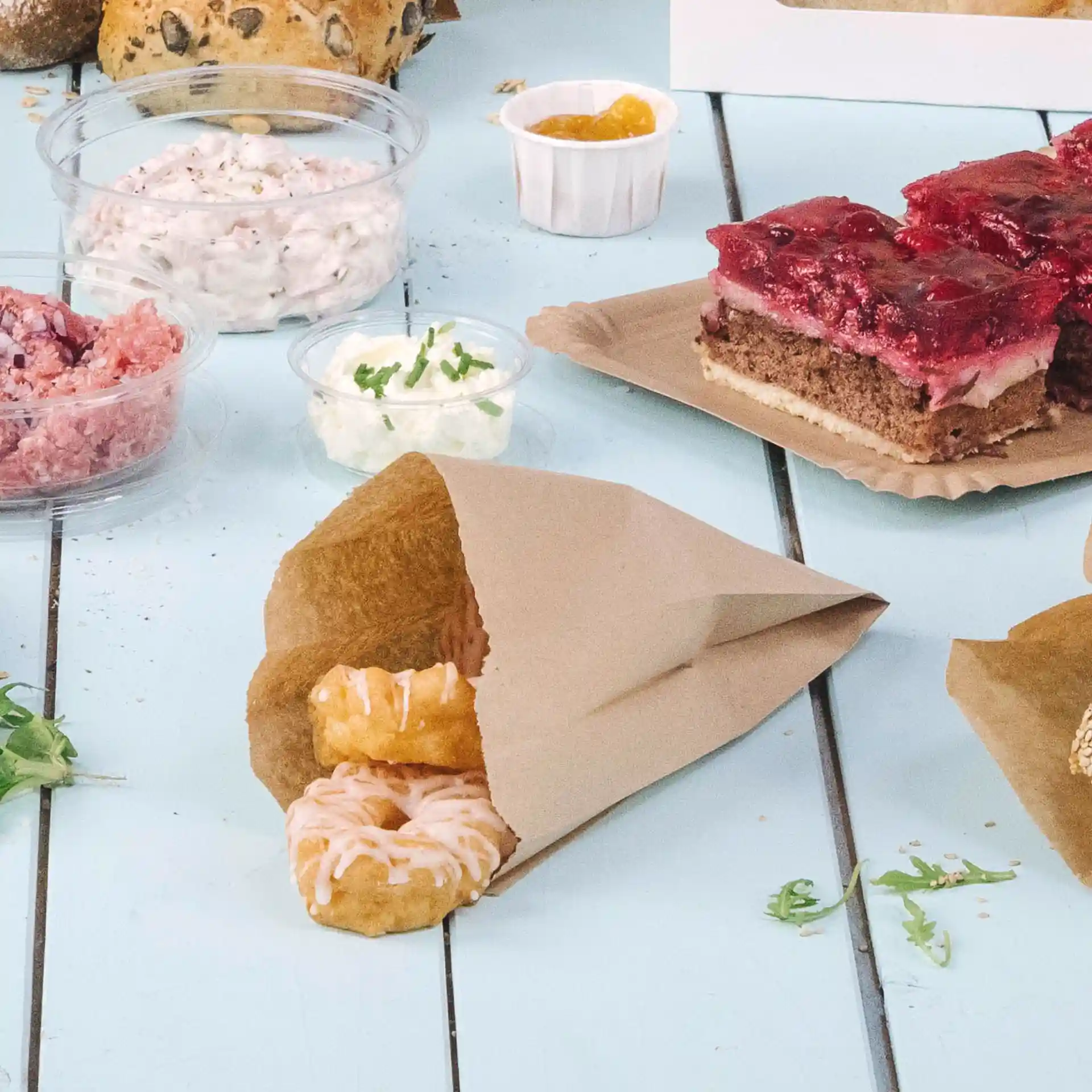 Brown flat paper bag containing two iced donuts, with various food items and containers in the background.