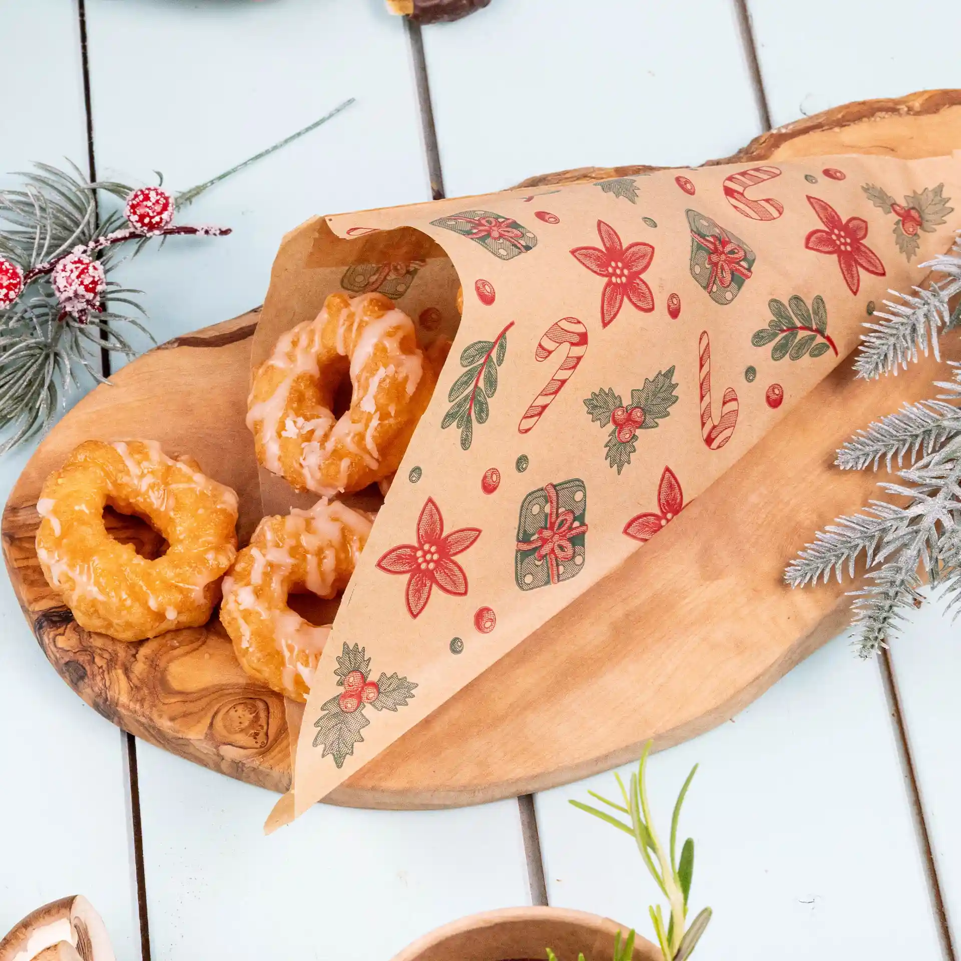 Brown greaseproof bag with winter design, containing three glazed donuts on a wooden platter.