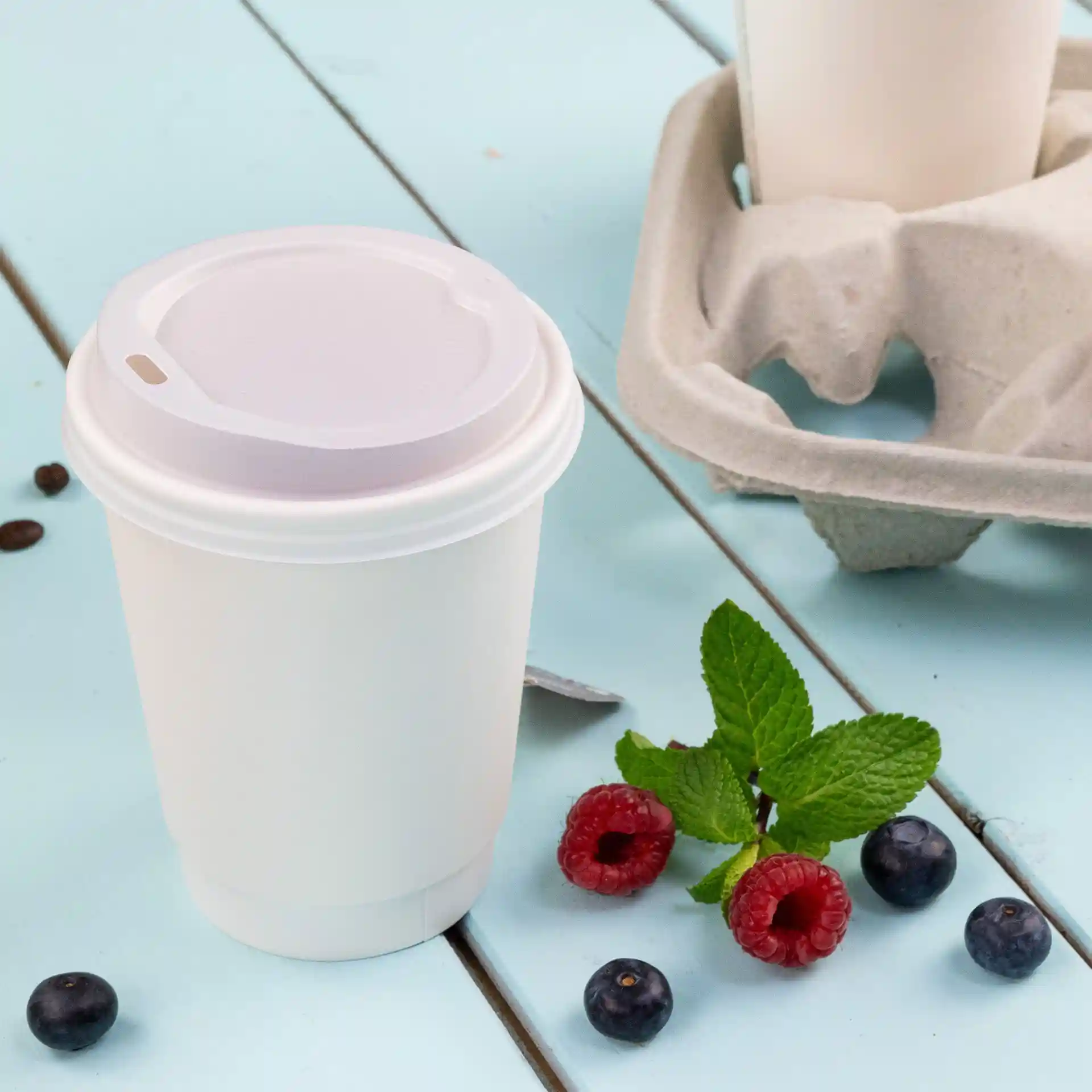 White double wall coffee cup with a lid, 300 ml, placed on a blue surface with raspberries, blueberries, and mint leaves.