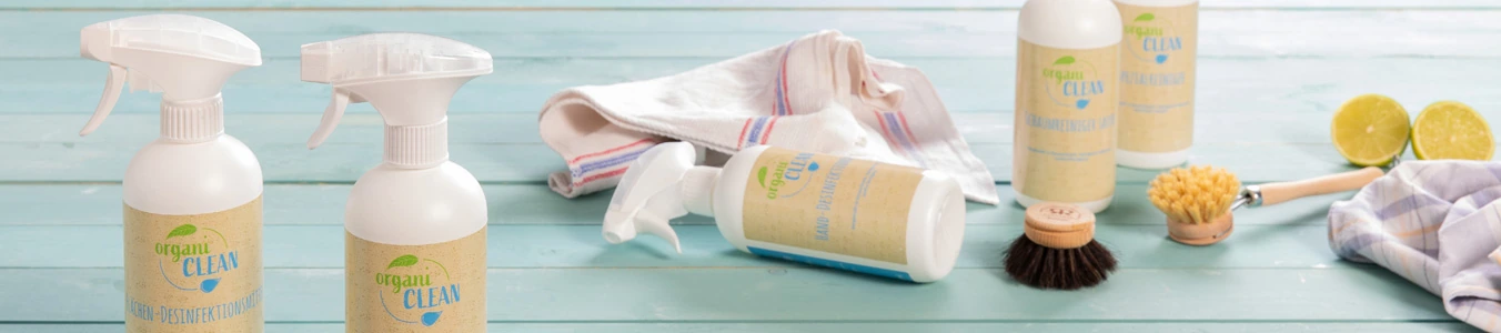 Two spray bottles of cleaning solution with labels, a cloth, a scrub brush, and halved limes on a blue wooden surface.