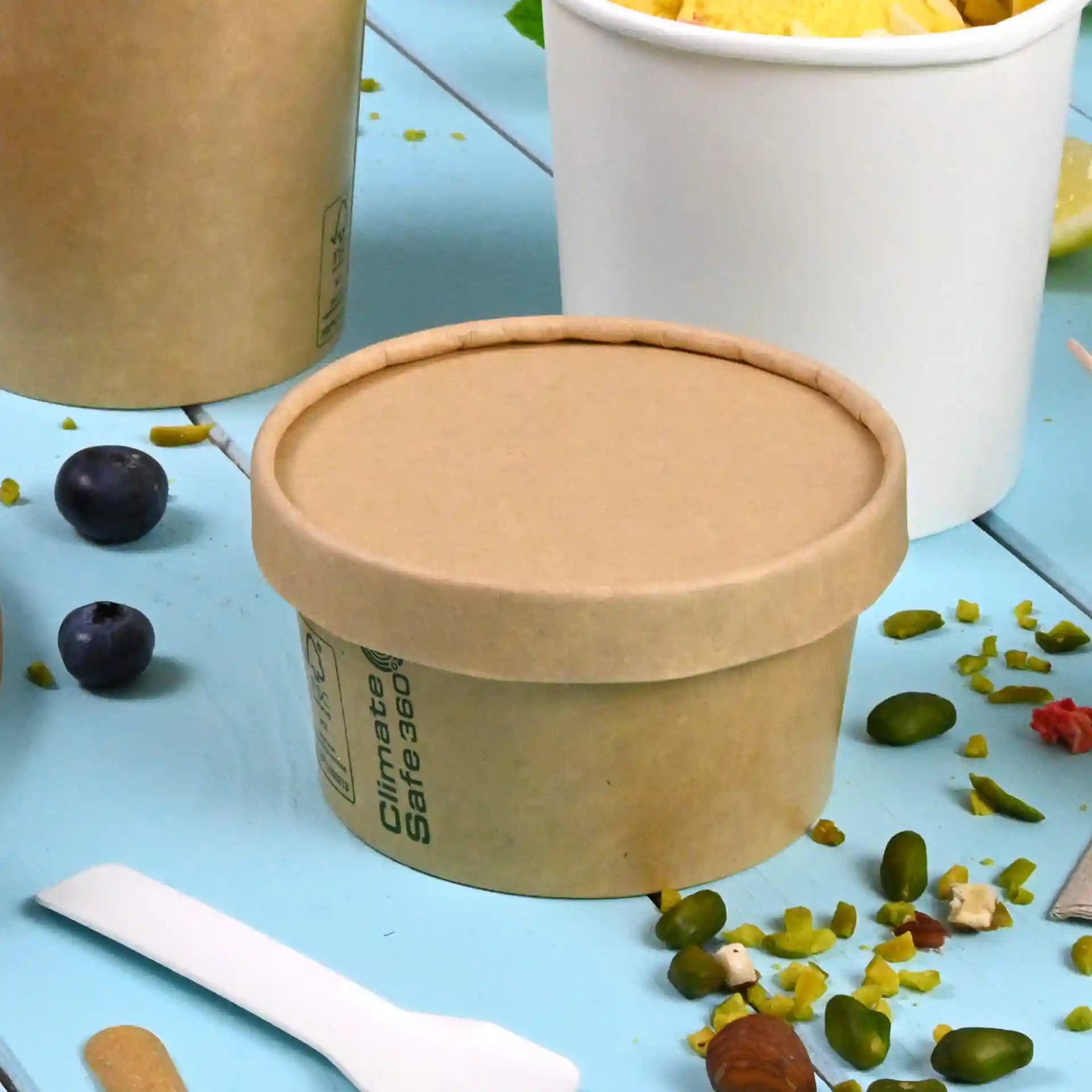 Brown cardboard lid with a round shape, designed for ice cream cups, placed on a blue surface with scattered food items.