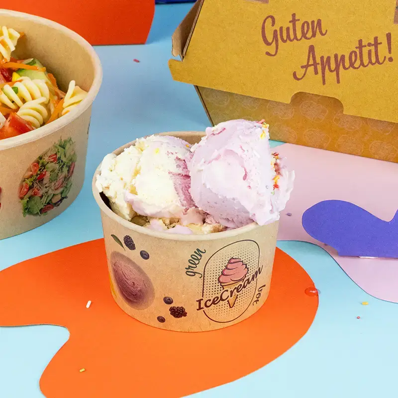 Green ice cream cup filled with multiple scoops of ice cream, topped with fruit and nuts, on a light blue background.