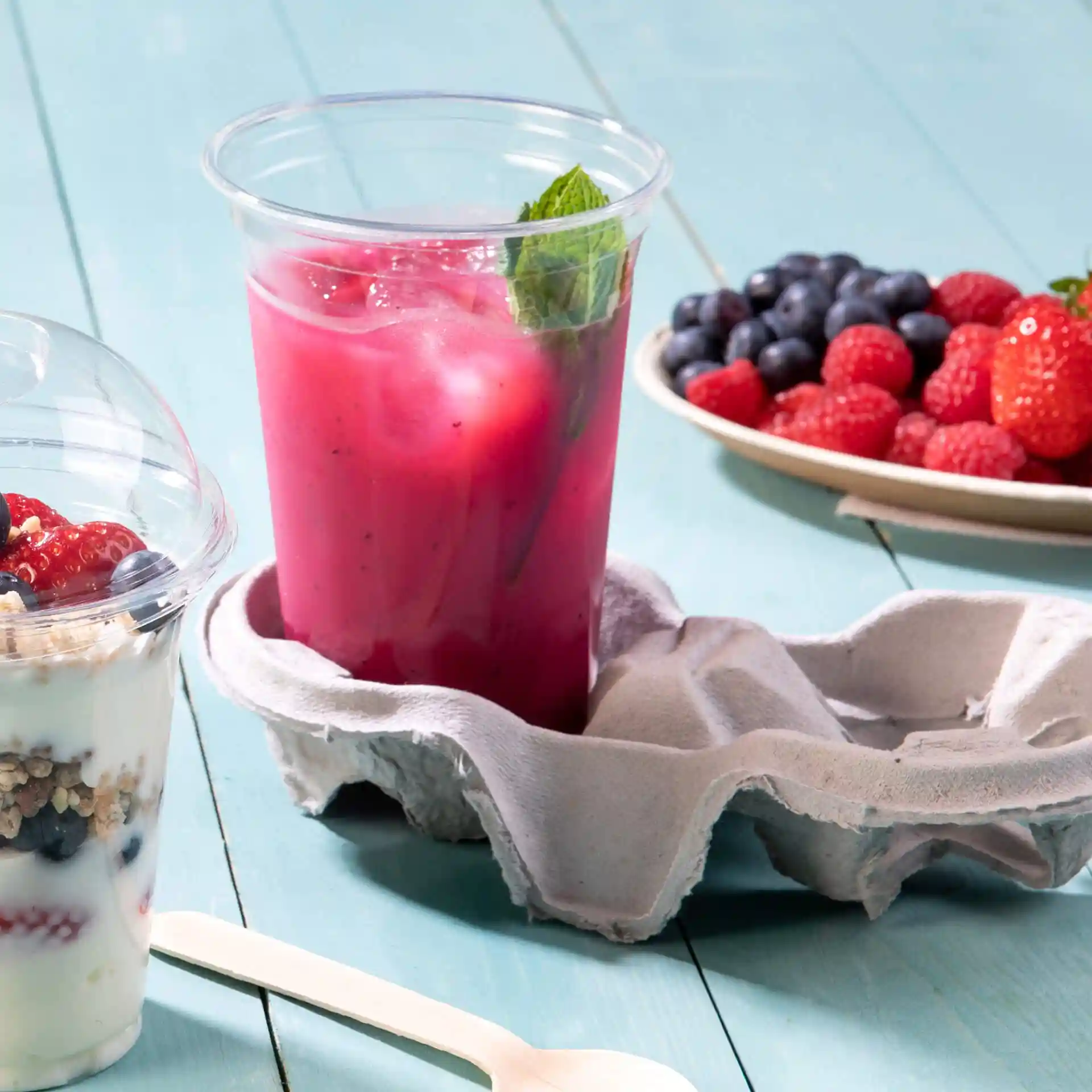 Clear 16 oz rPET cup filled with a pink drink and mint, placed in a gray egg carton holder with a yogurt parfait nearby.