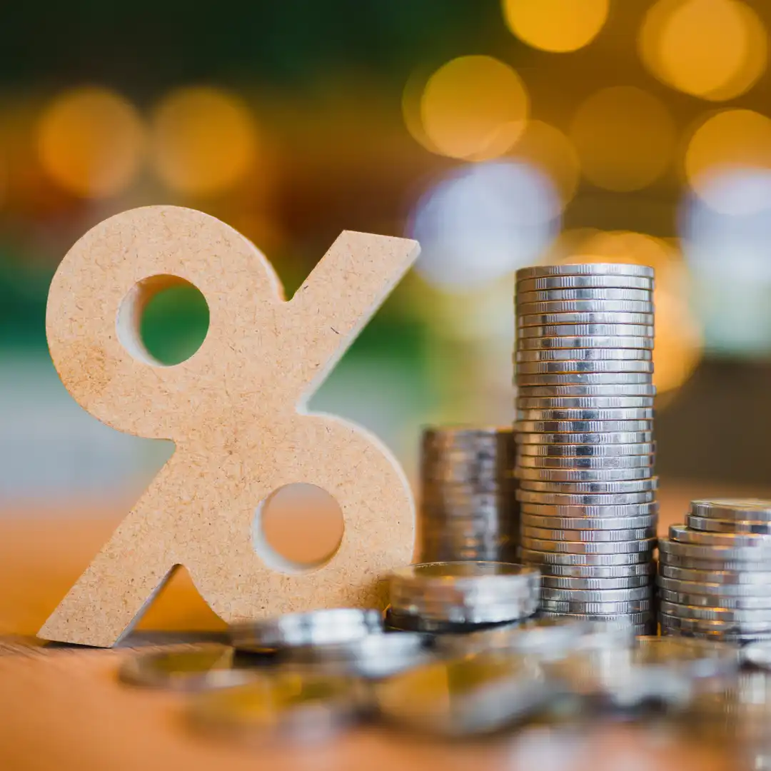 Wooden percentage symbol next to stacks of silver coins on a blurred background.