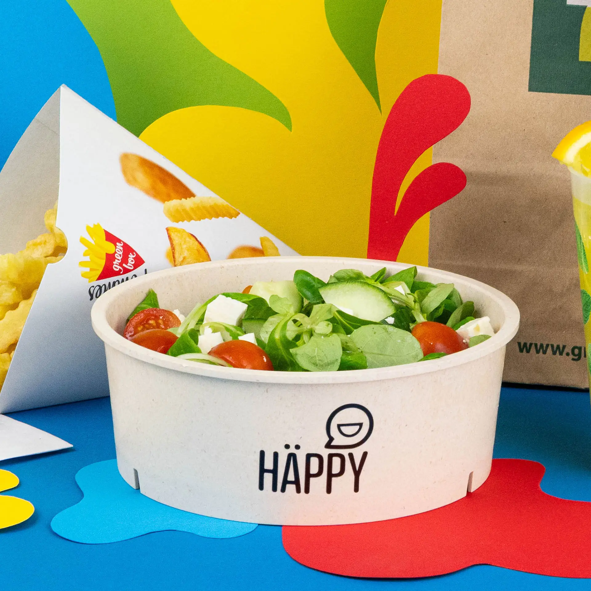 Reusable cream-white bowl filled with salad including lettuce, tomatoes, and feta, with printed branding on the side.