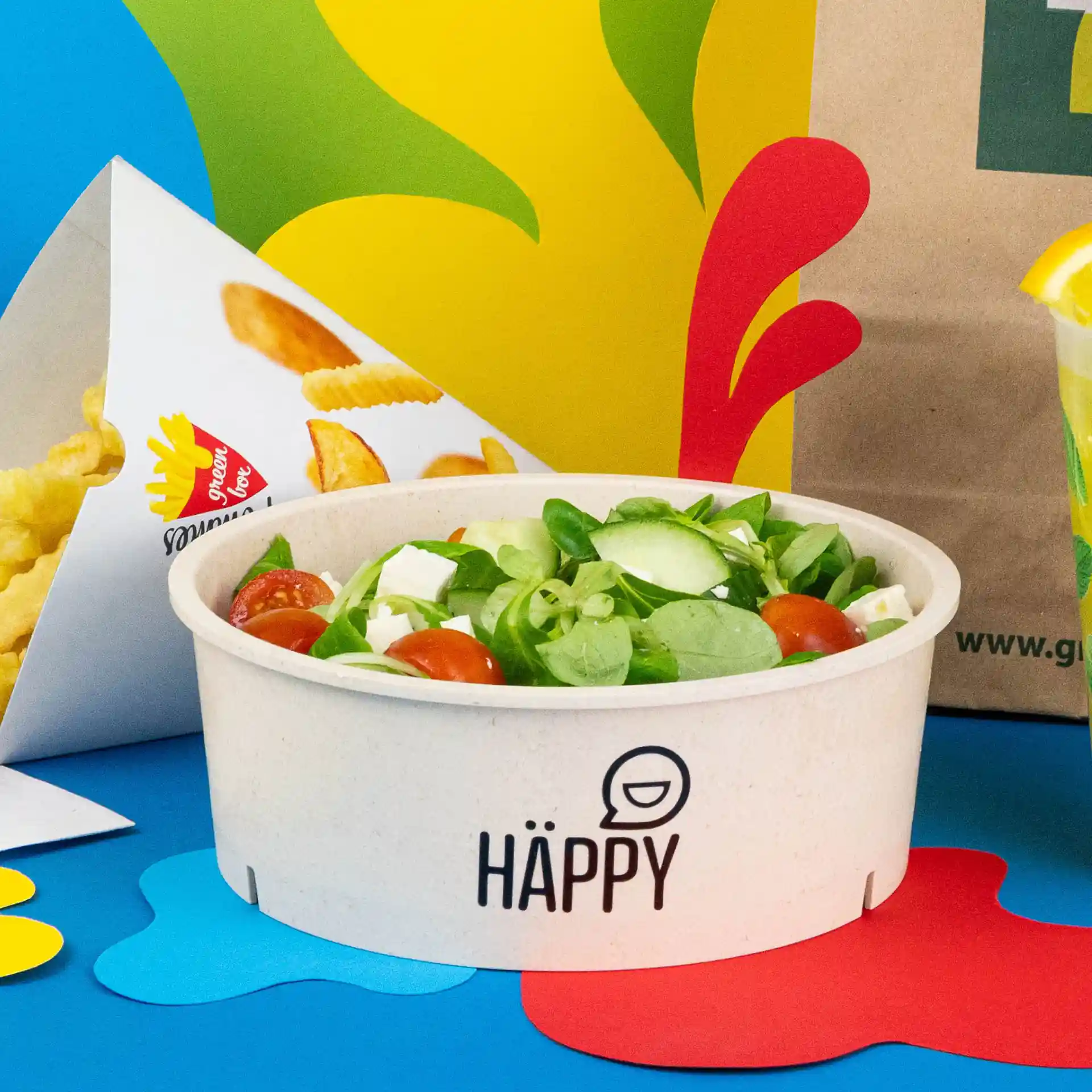 Round reusable bowl with salad, cream-white color, on a blue background with other food items.
