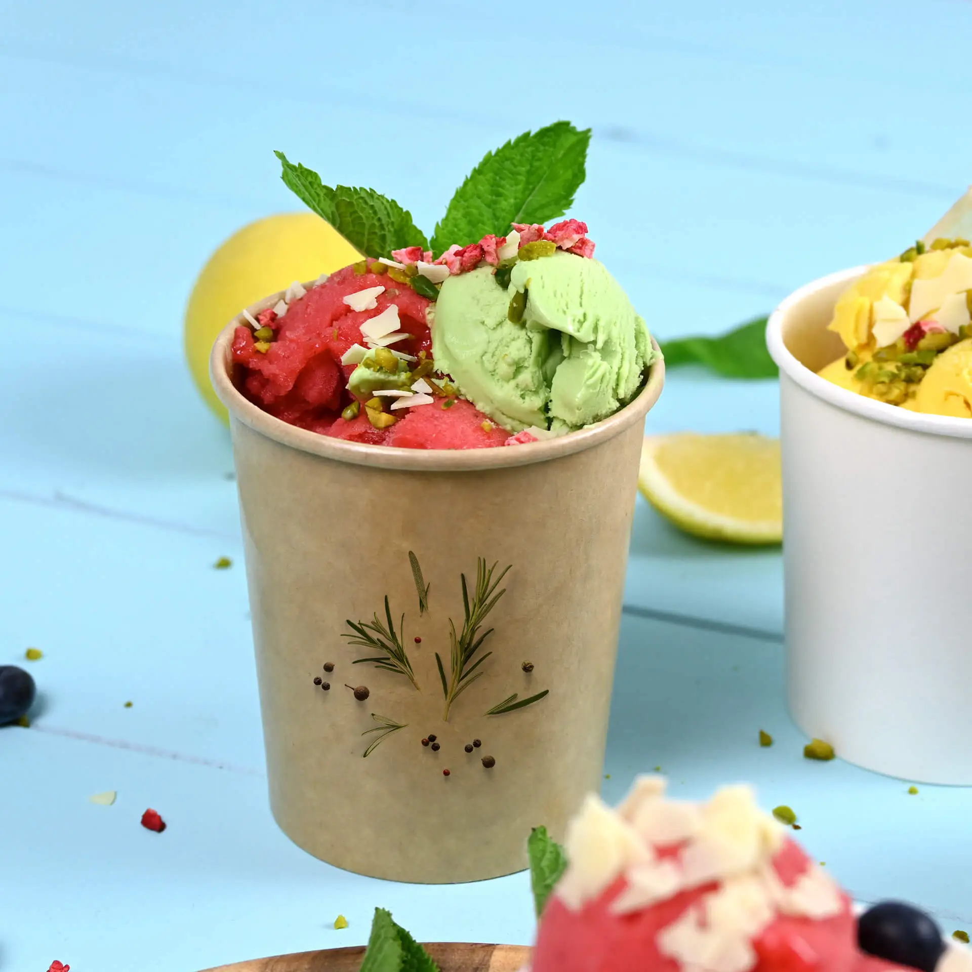 Brown ice cream cup filled with red and green ice cream, topped with nuts and mint leaves, on a blue background.
