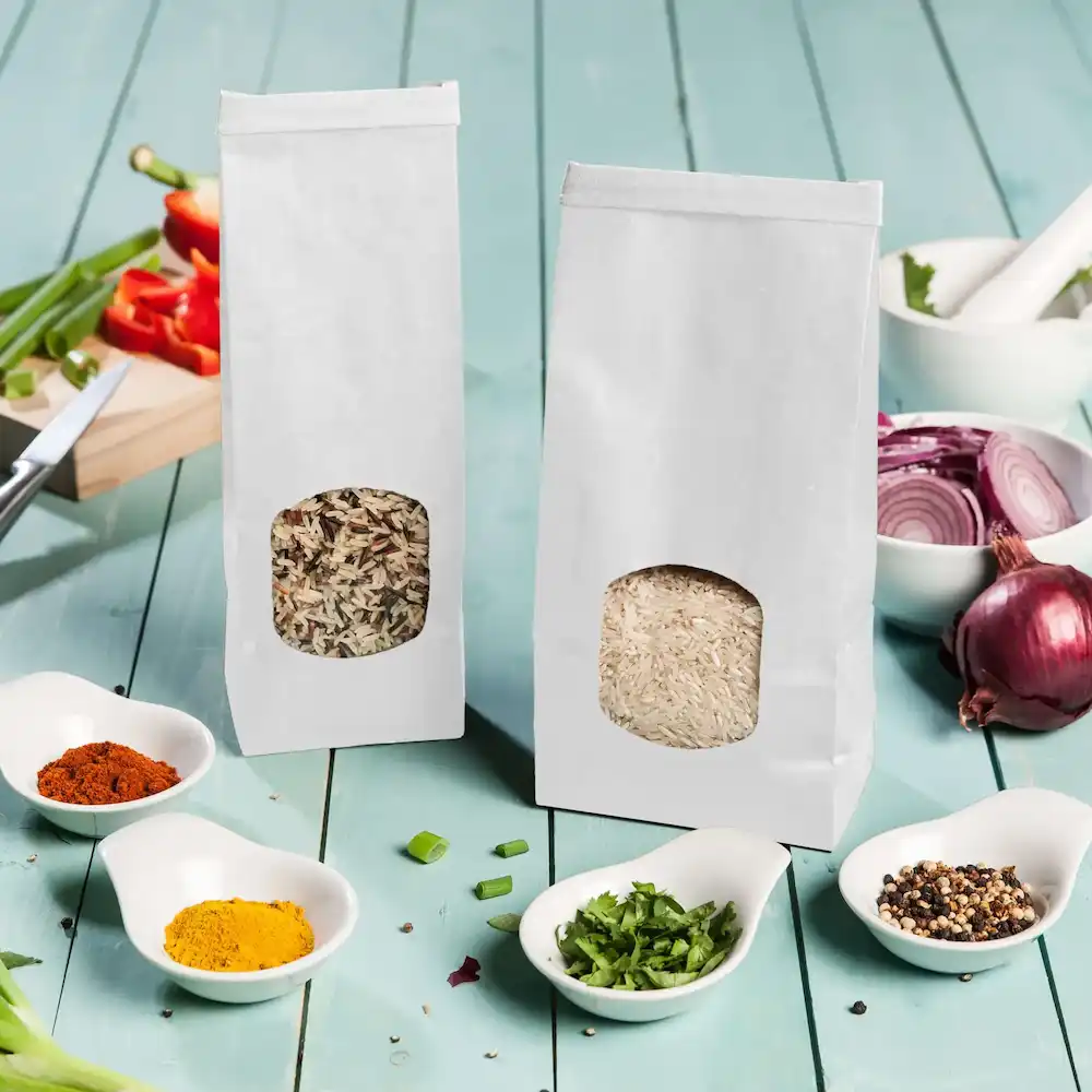 Two white paper bags containing rice and a mix of grains, surrounded by small dishes of spices and chopped vegetables.