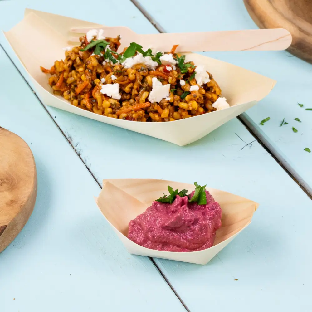 Bamboo serving trays with mixed vegetable dish and pink dip, garnished with herbs, on a light blue wooden surface.