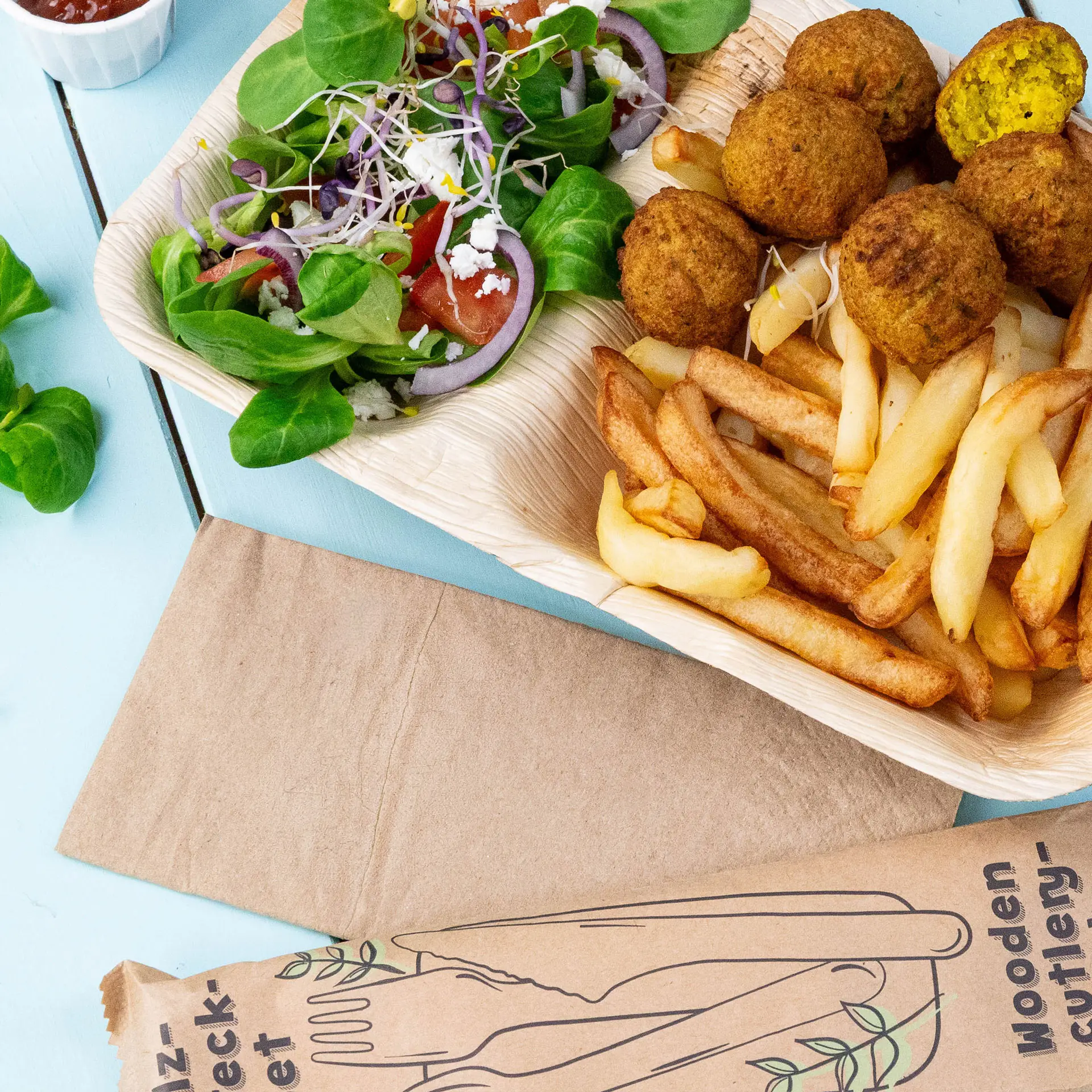 Image of a wooden tray containing falafel balls, French fries, and a mixed salad with greens, tomatoes, and onions.