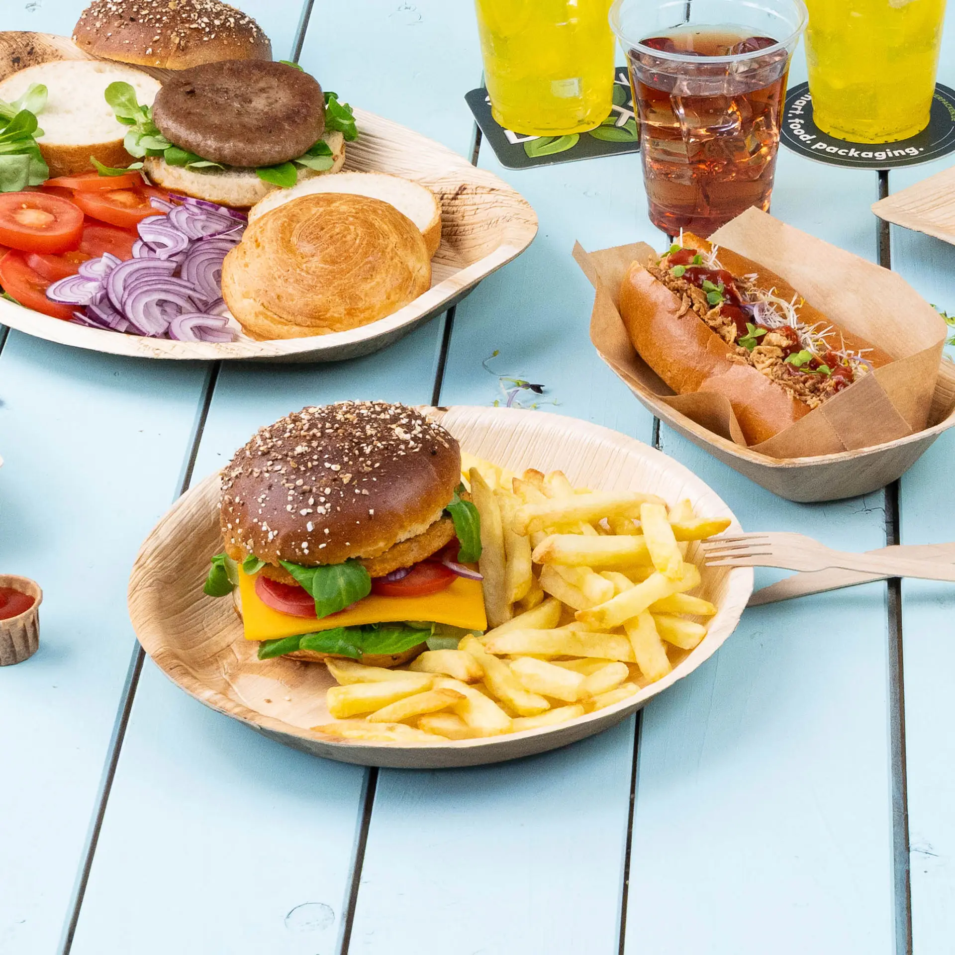 Round palm leaf plate with a hamburger topped with cheese, lettuce, and tomato, served with fries on a blue table.