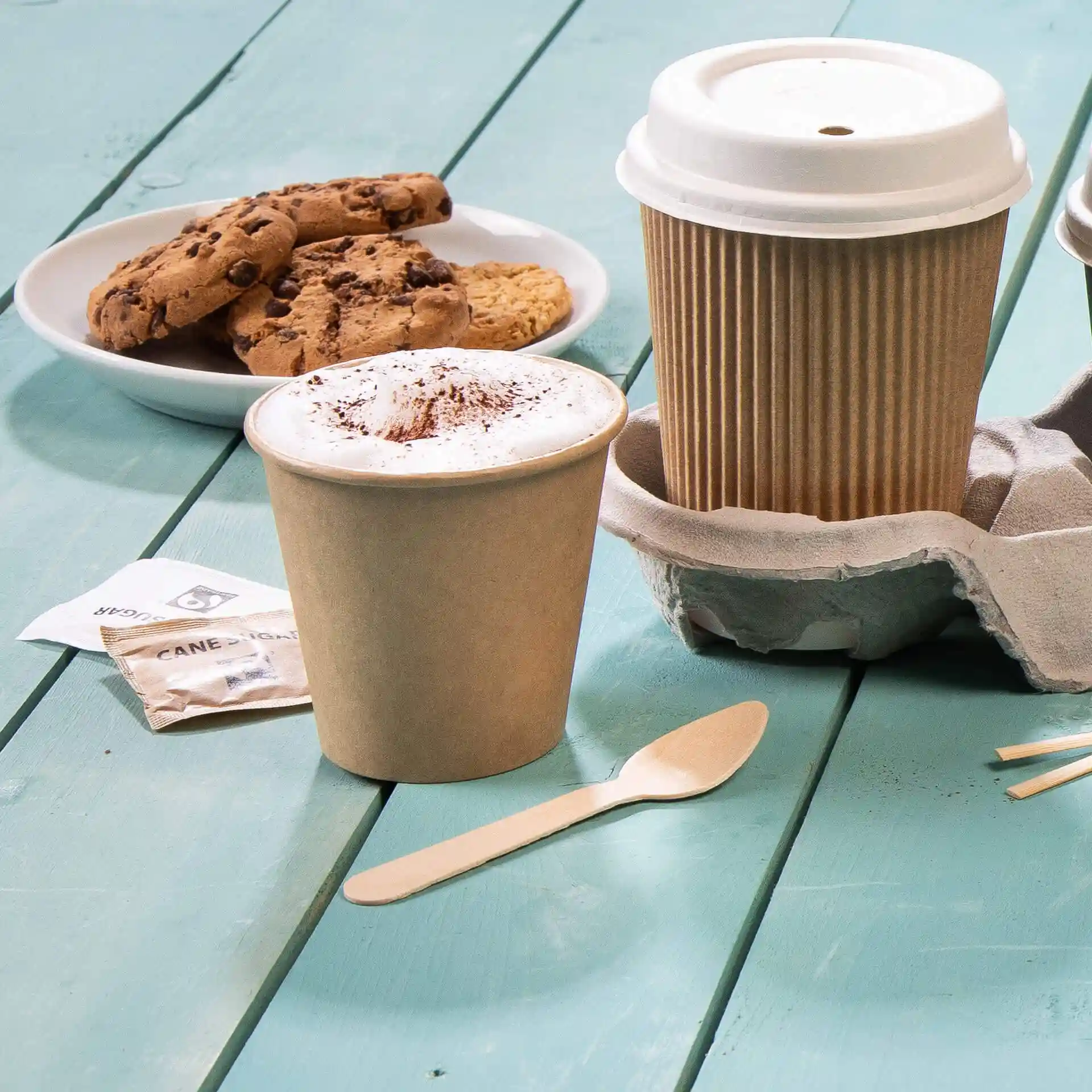 Brown wooden espresso spoon next to a coffee cup and cookies on a blue wooden surface.