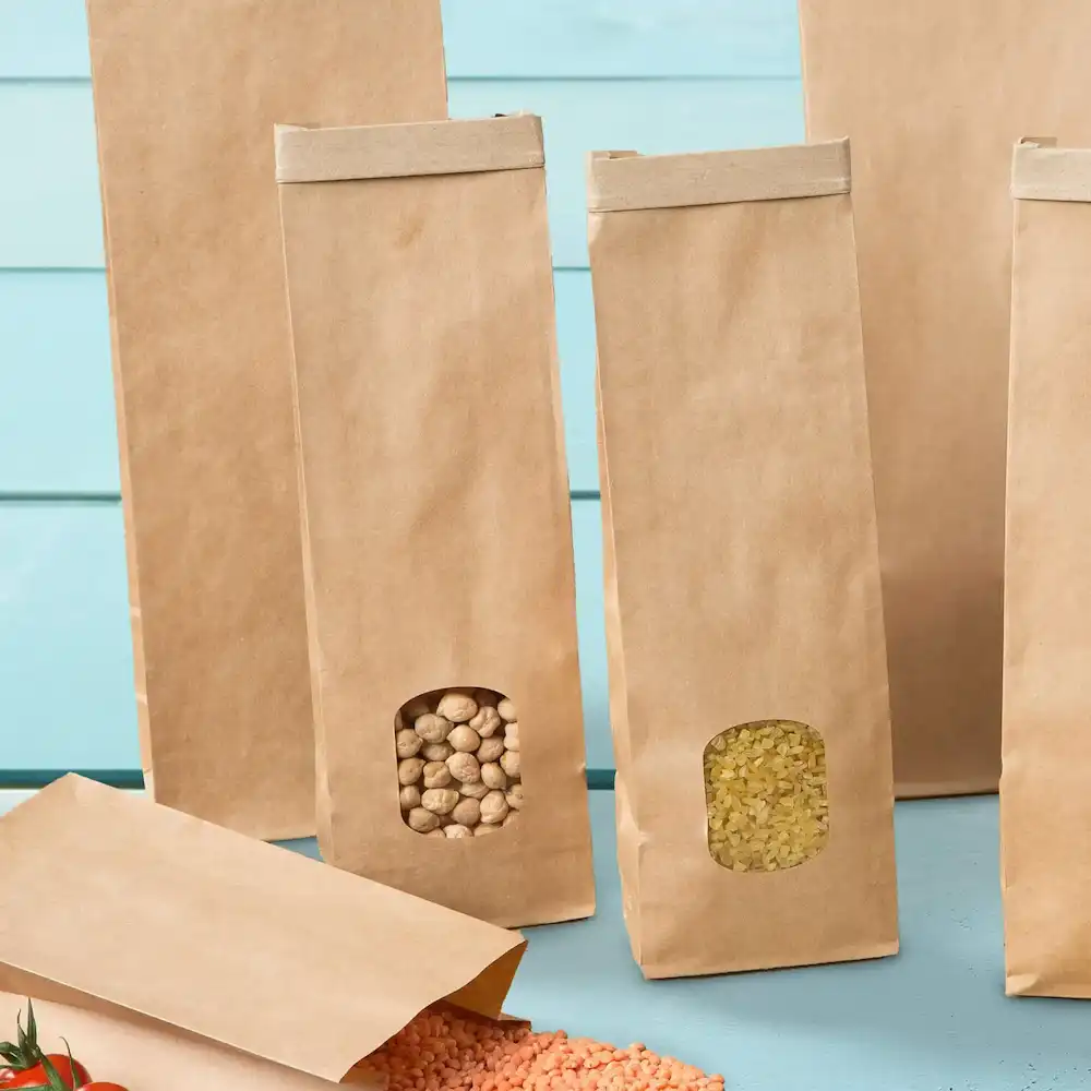 Brown block-bottom bags with transparent windows displaying contents, placed on a light blue surface.