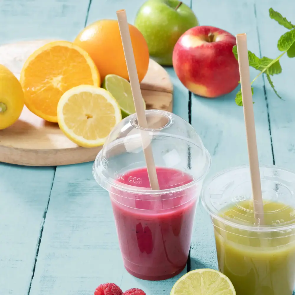 Two transparent cups with fruit smoothies, one pink and one green, placed next to fresh fruits on a blue surface.