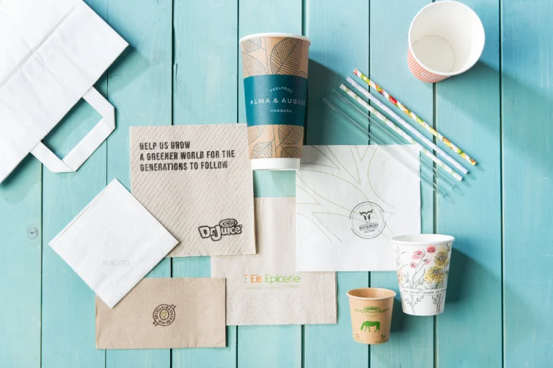 Various packaging items including paper cups, napkins, and straws on a turquoise wooden surface.