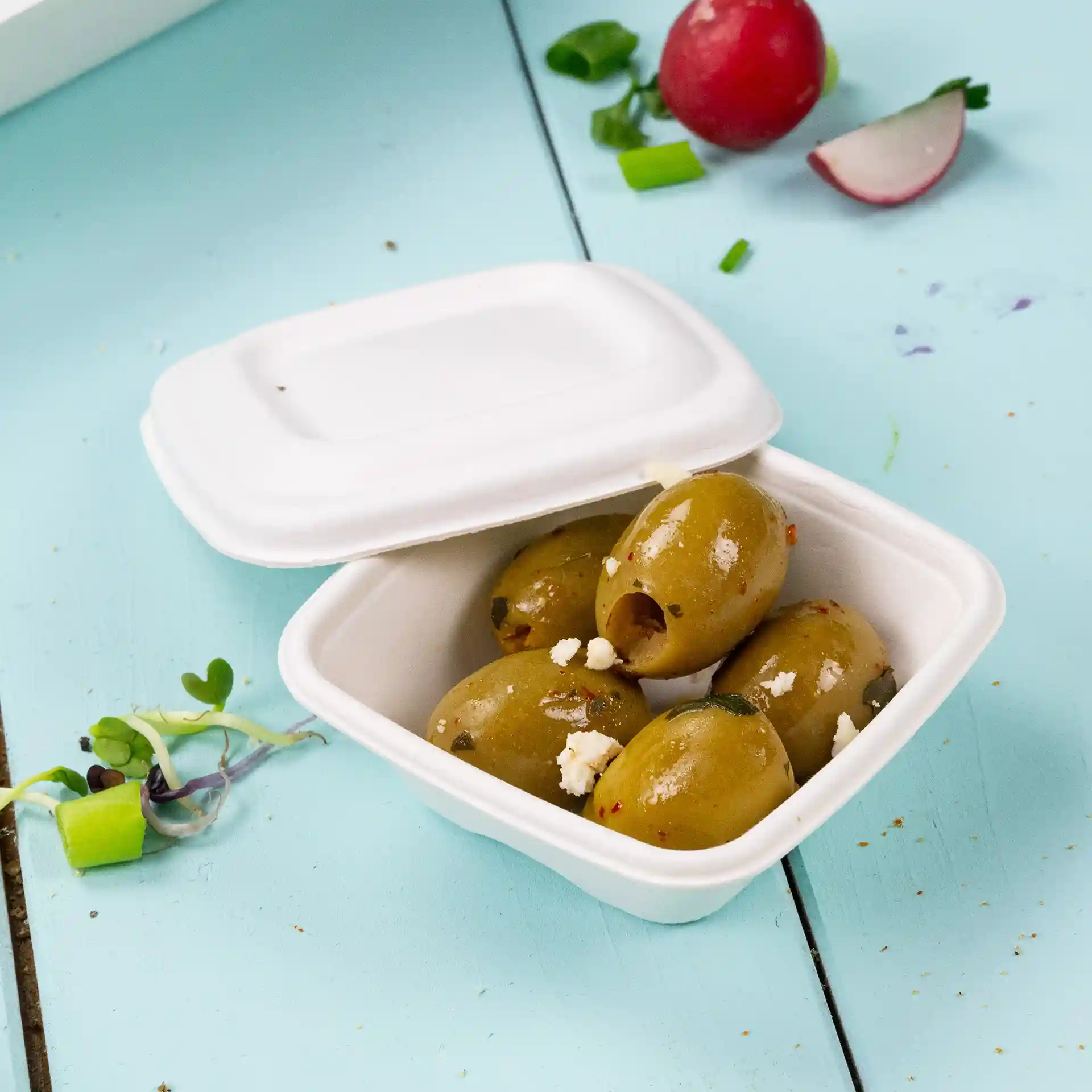 Container with five green olives inside, placed on a light blue surface, with a white lid partially closed.