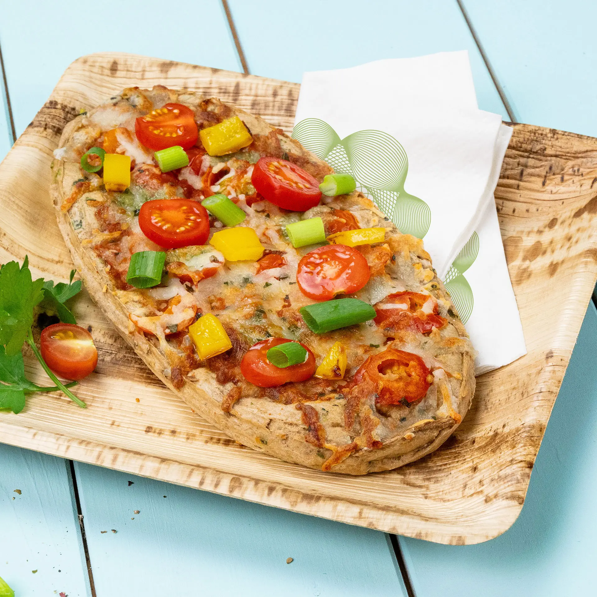 Vegetable pizza topped with cherry tomatoes, green onions, and yellow bell peppers on a wooden plate with a napkin.