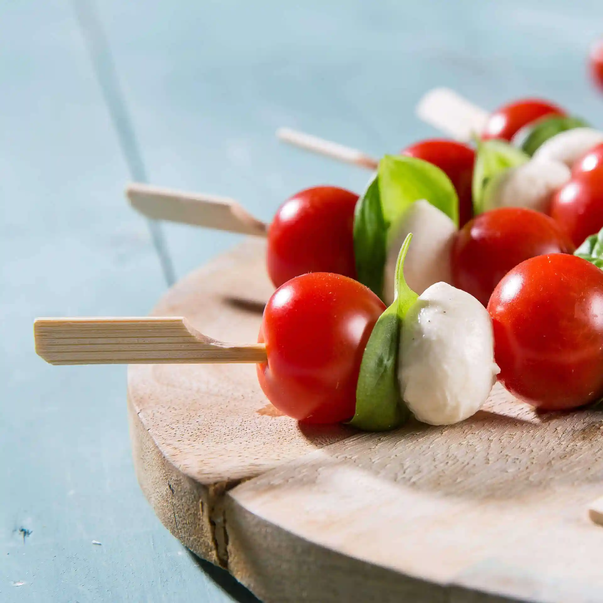 Skewers with cherry tomatoes, basil, and mozzarella on a wooden serving board.