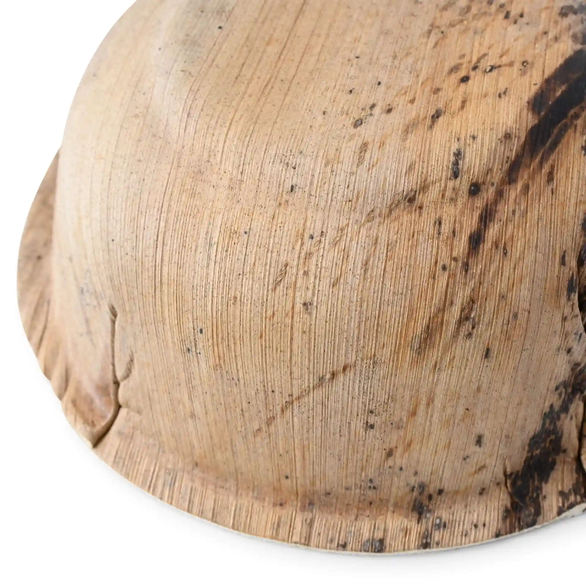 Close-up of a round palm leaf bowl with a textured grain surface and a slight dark mark.