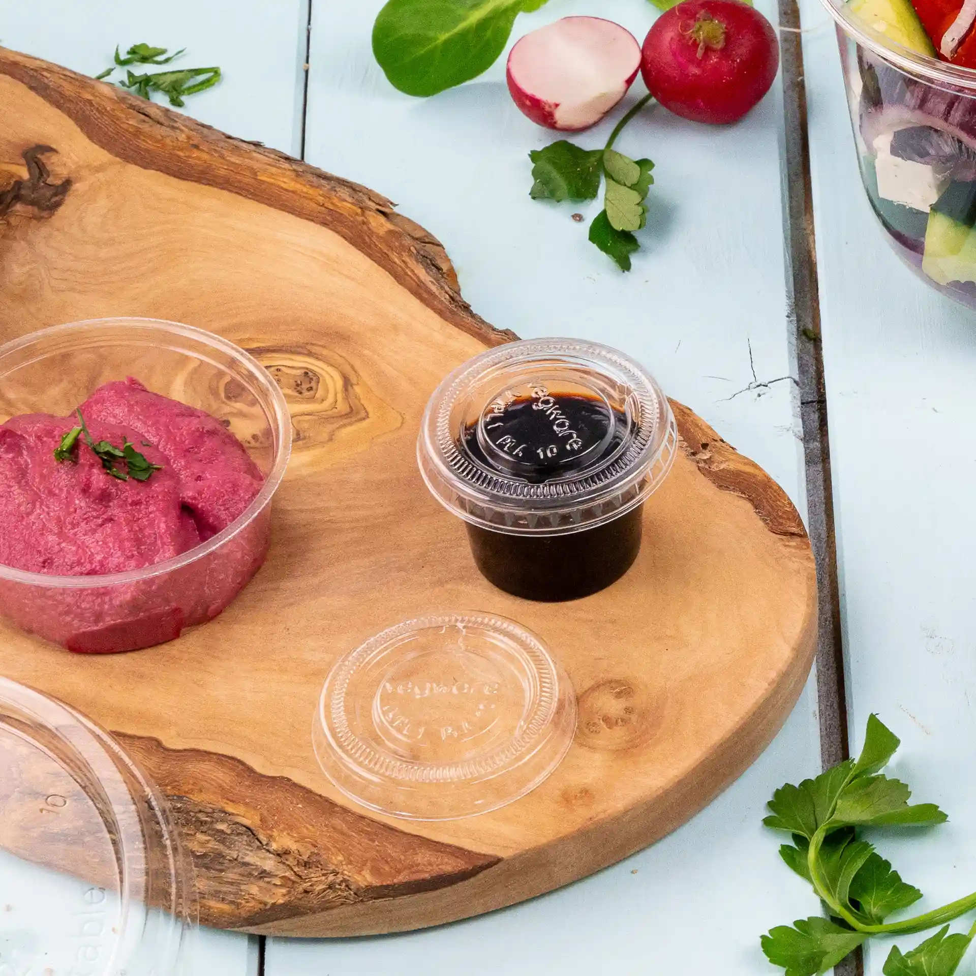 Image of a wooden serving board with a pink dip in a clear container and a dark sauce in another clear container.