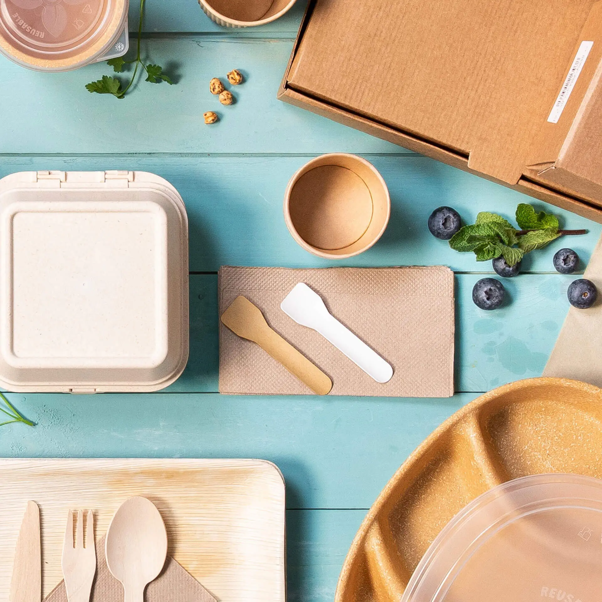 Image of various disposable food containers, utensils, and a cardboard box on a blue surface.