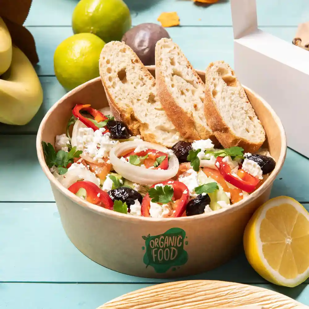 Bowl of salad with vegetables, cheese, and herbs, accompanied by slices of bread, on a colored tabletop.