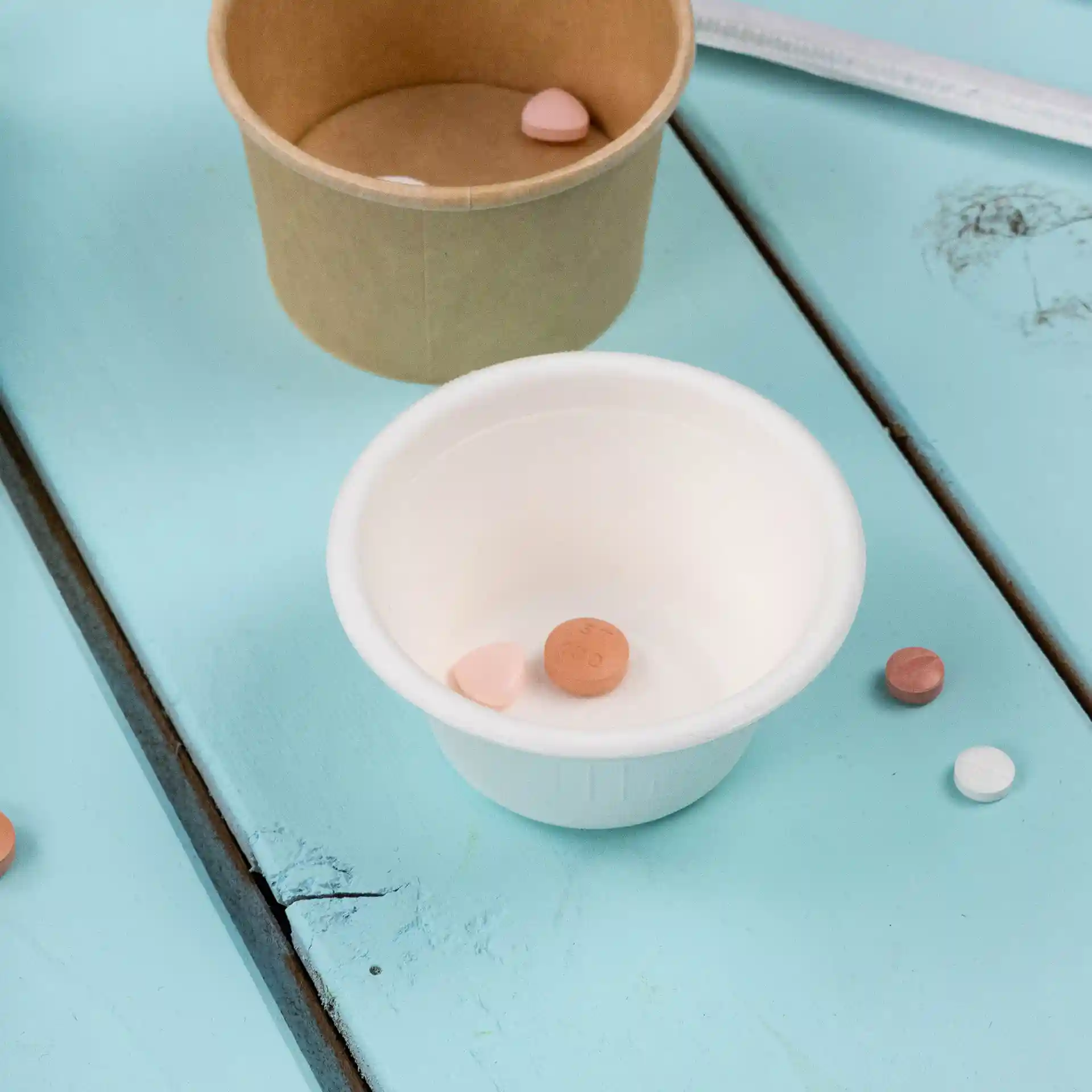White bagasse dip bowl with a diameter of 62 mm, containing several small pills on a blue wooden surface.