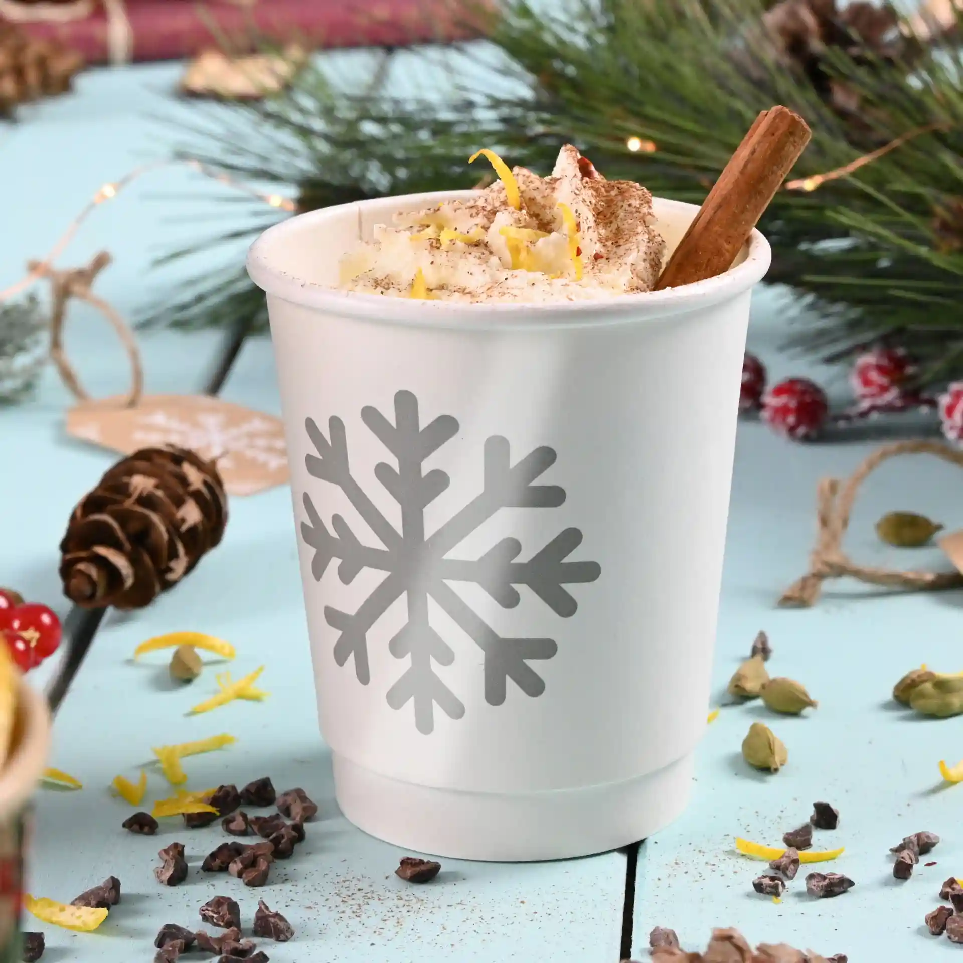 White double-walled paper cup with a gray snowflake design, filled with whipped cream and garnished with a cinnamon stick.