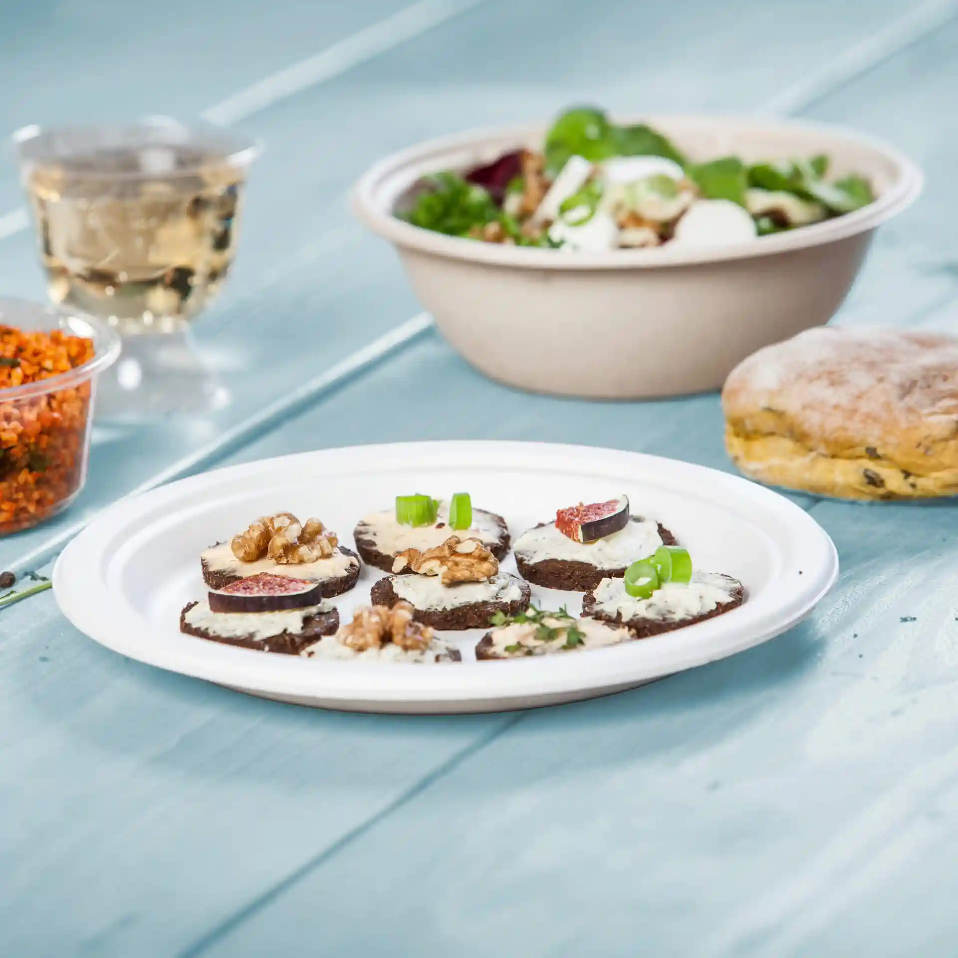 Plate with several round slices of dark bread topped with cream, walnuts, and figs, alongside a salad and a biscuit.
