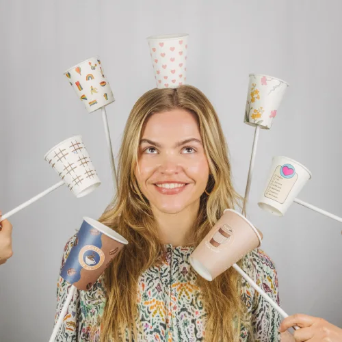Woman with long hair smiling and holding several colorful paper cups on sticks around her head.
