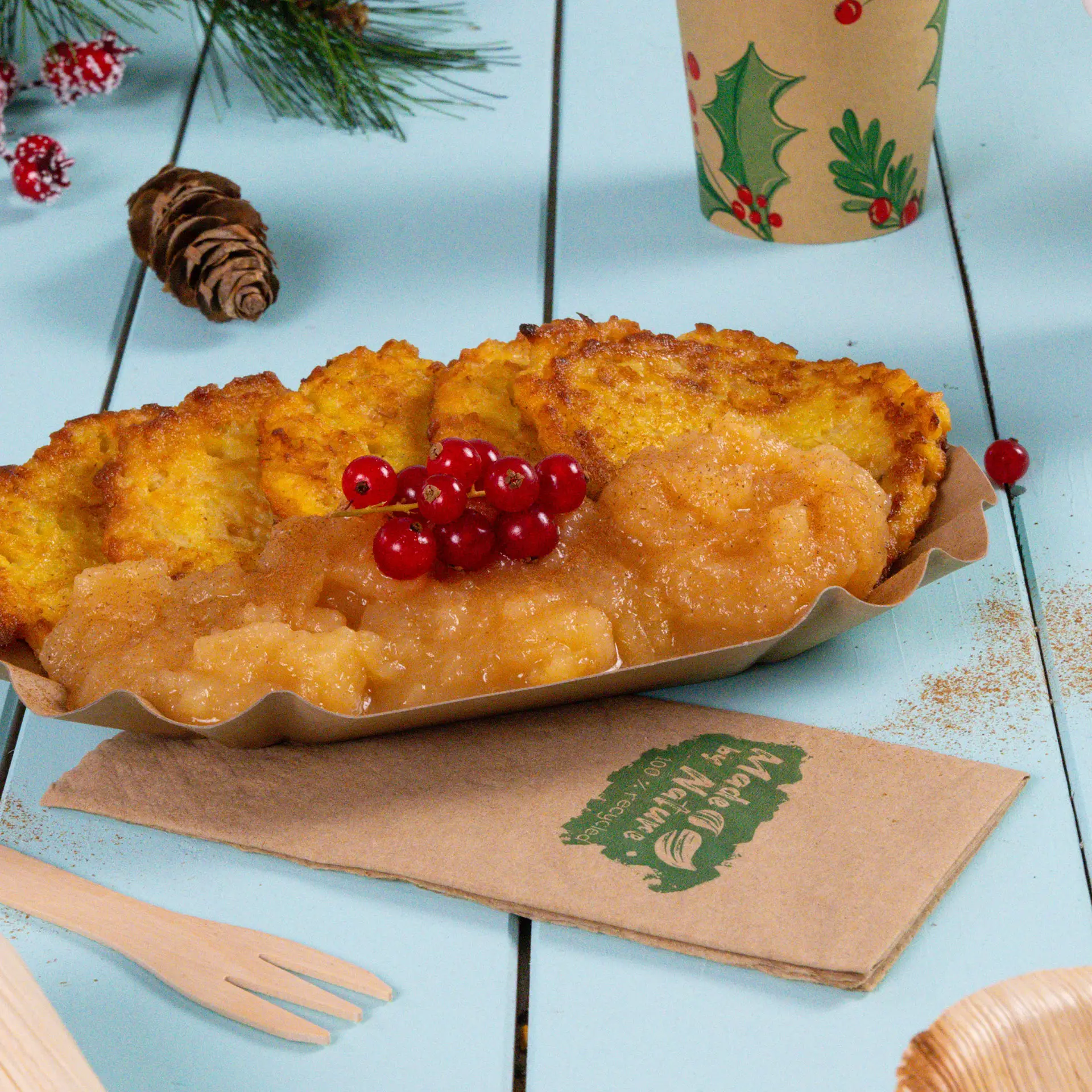 One plate of crispy potato pancakes served with applesauce and garnished with red currants, beside a paper napkin and decorative elements.