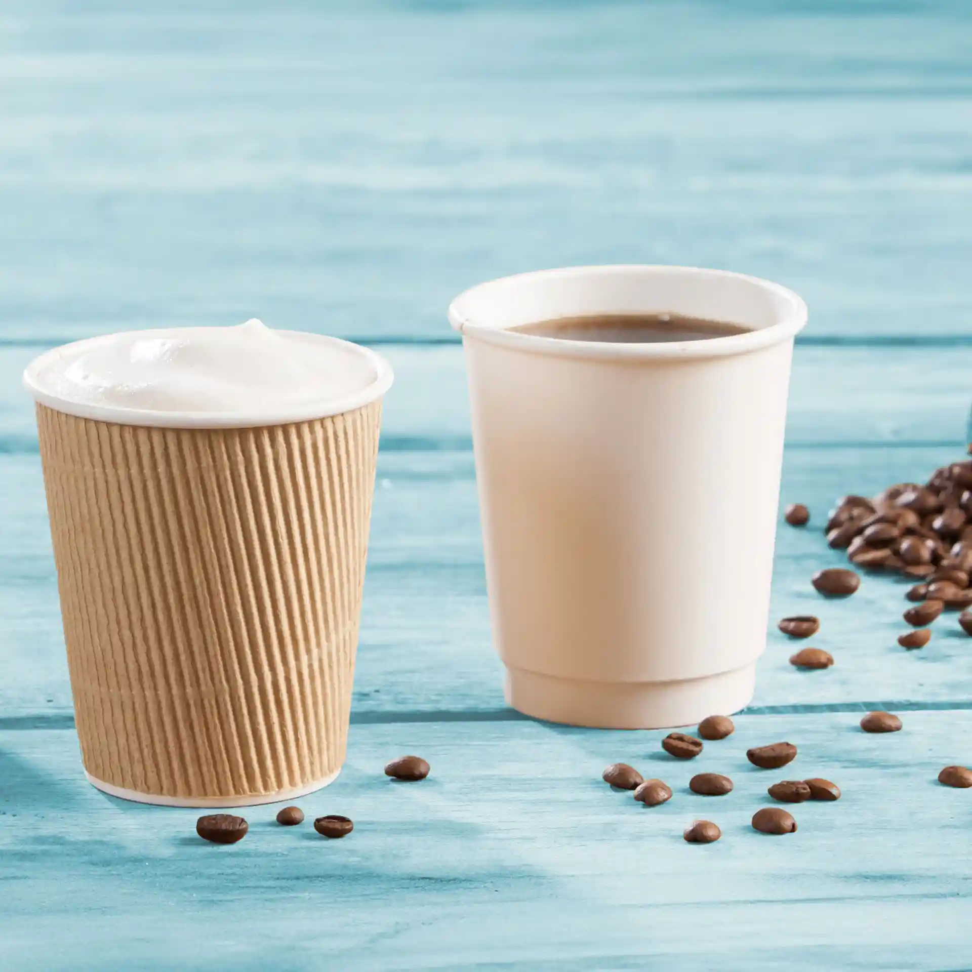 Double-walled cardboard coffee cups in brown and white, with coffee beans scattered on a blue wooden surface.